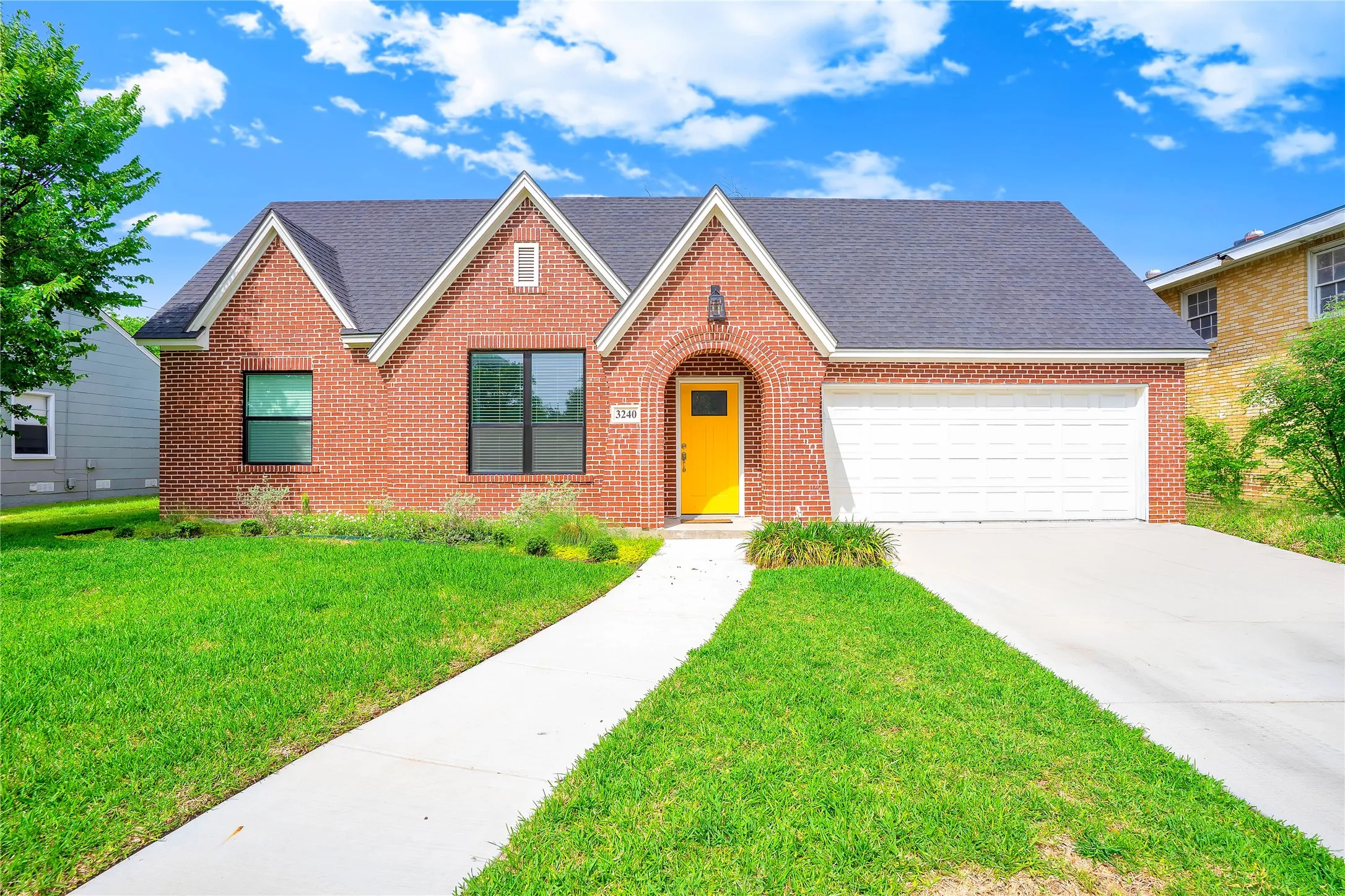 Brick facade residence featuring a prominent yellow front door, arched entryway, dark roof, and an attached two-car garage