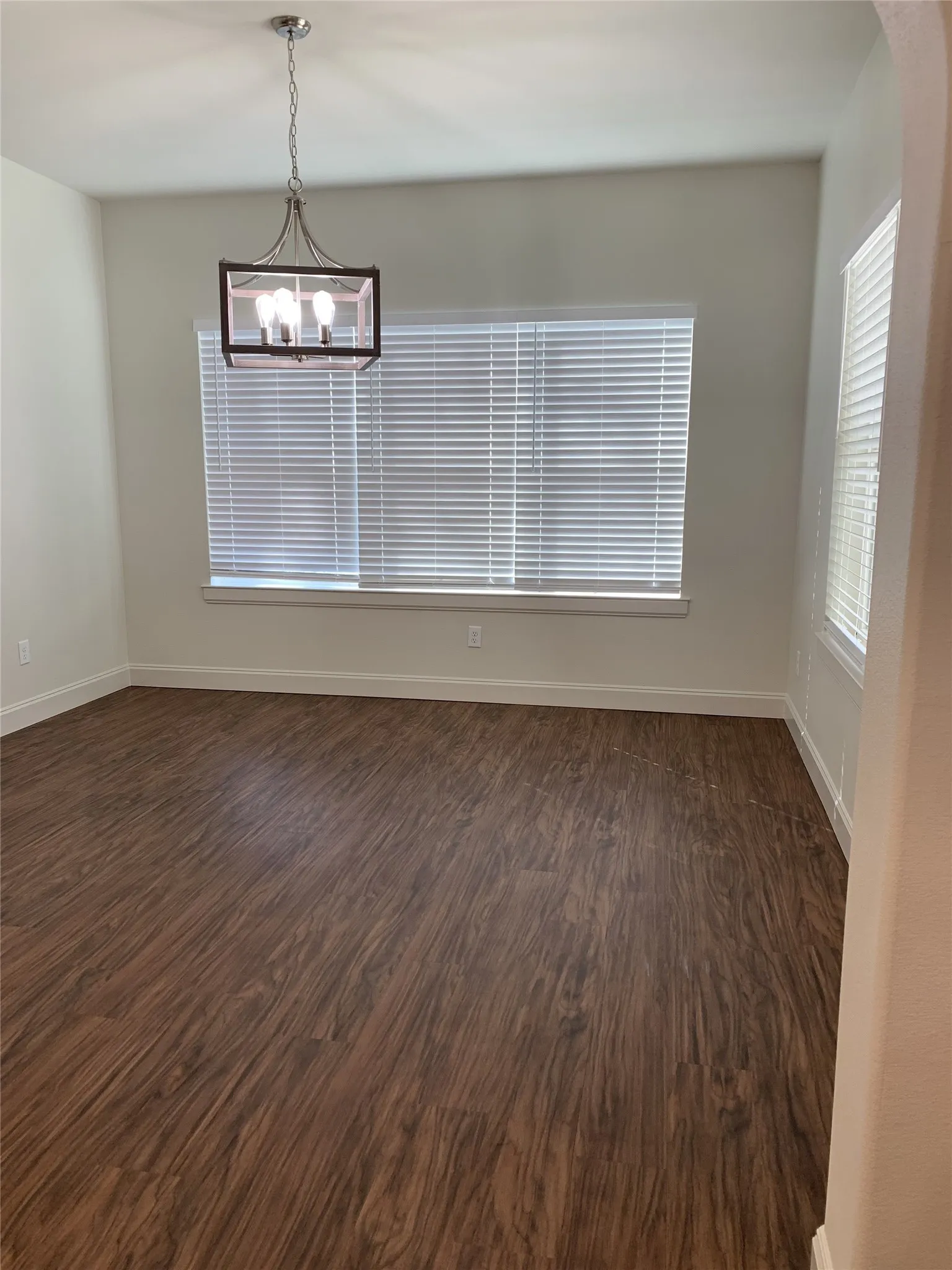 Spacious room featuring wood-finish flooring, a contemporary chandelier, and multiple windows with blinds