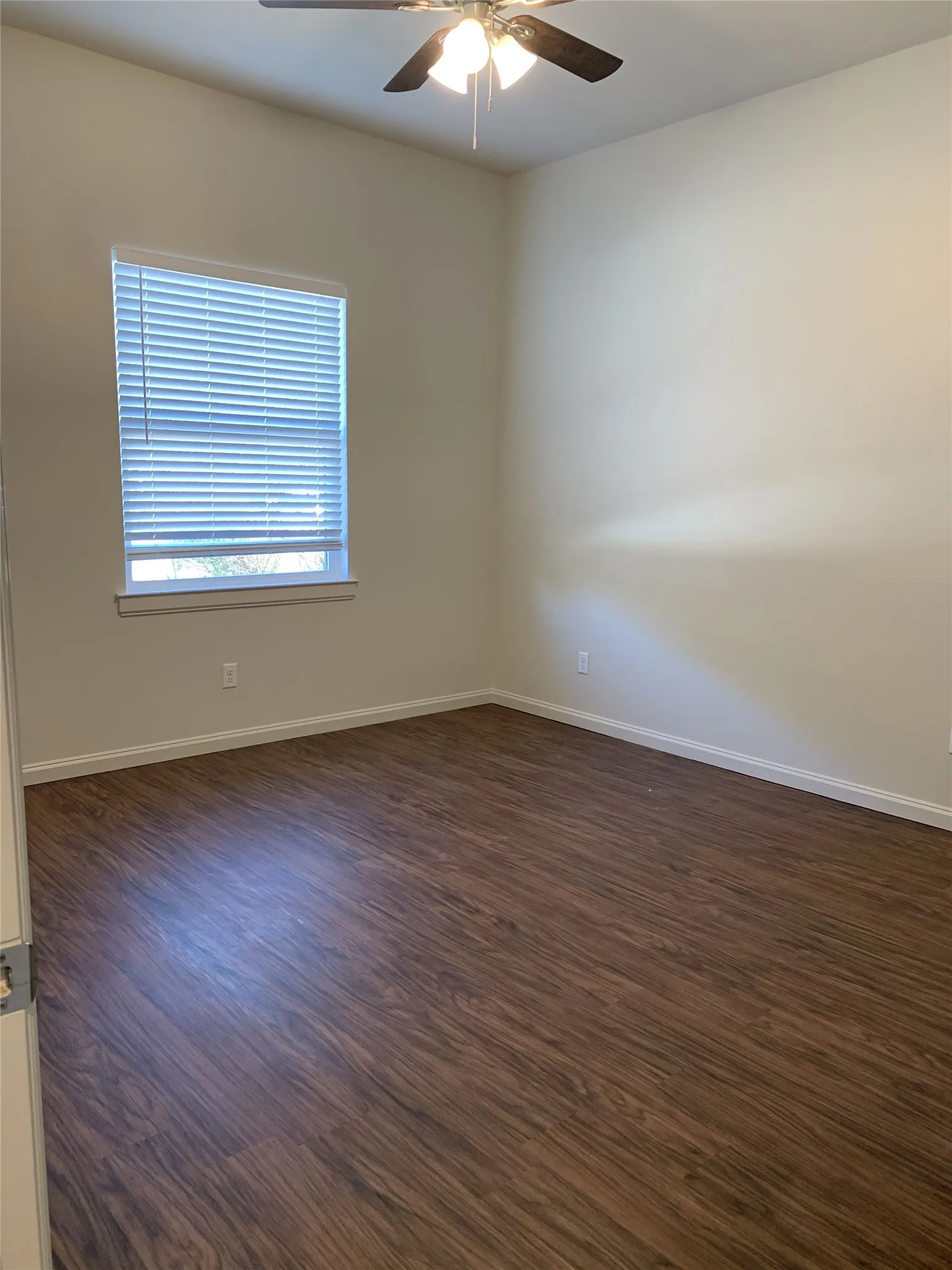 Room featuring wood-finish flooring, a ceiling fan with integrated lighting, a window with blinds, and neutral-toned walls
