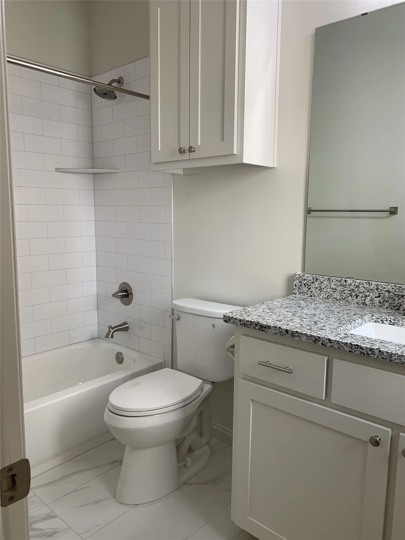 Bathroom featuring a white subway tile tub surround, white vanity with a granite-style countertop, integrated sink, and white shaker-style cabinetry