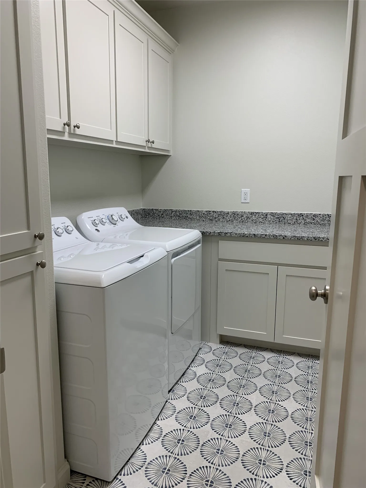 Laundry area featuring patterned floor tiles, white shaker cabinetry, a speckled countertop, and brushed nickel hardware
