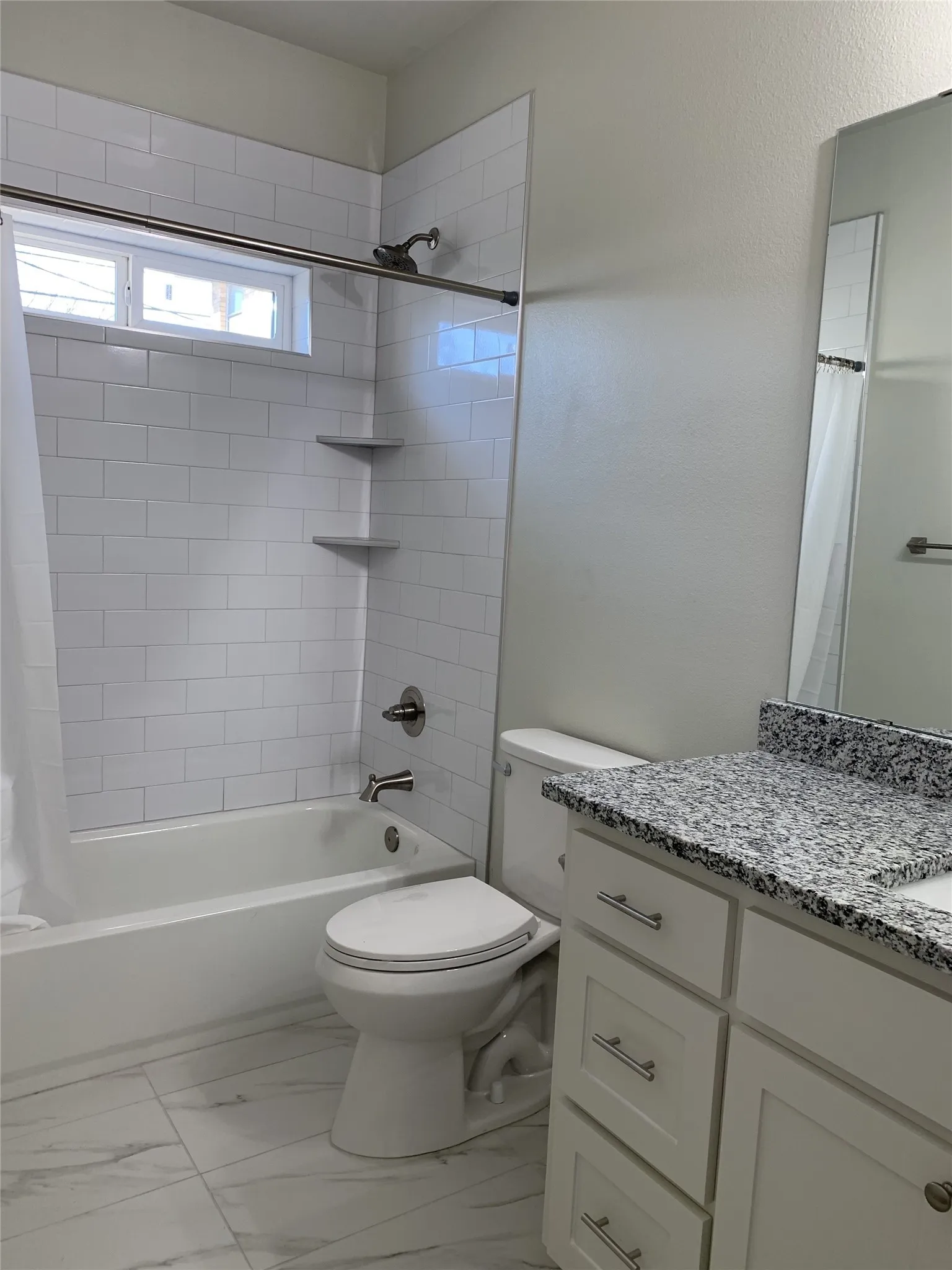 Bathroom featuring a white subway tile shower surround with built-in corner shelves, a white bathtub, and a window above the tub