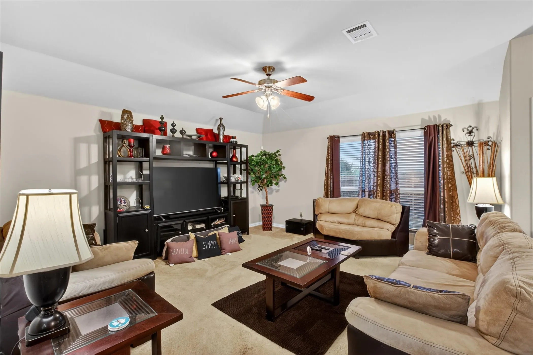 Spacious living area featuring neutral wall tones, carpeted flooring, and a ceiling fan