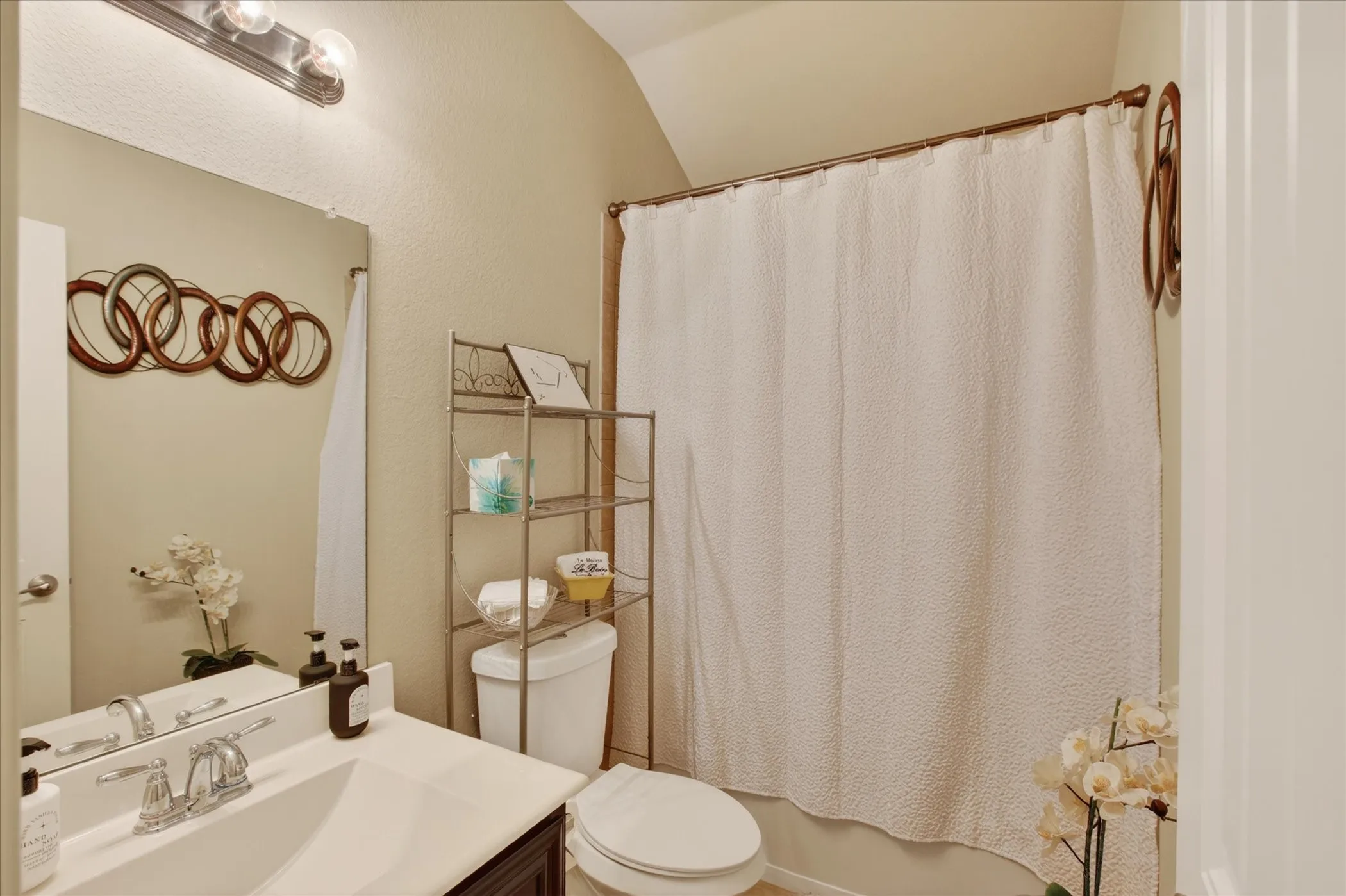 Bathroom featuring a vanity with an integrated sink, a large wall-mounted mirror, and a shower-tub combination with a curtain rod