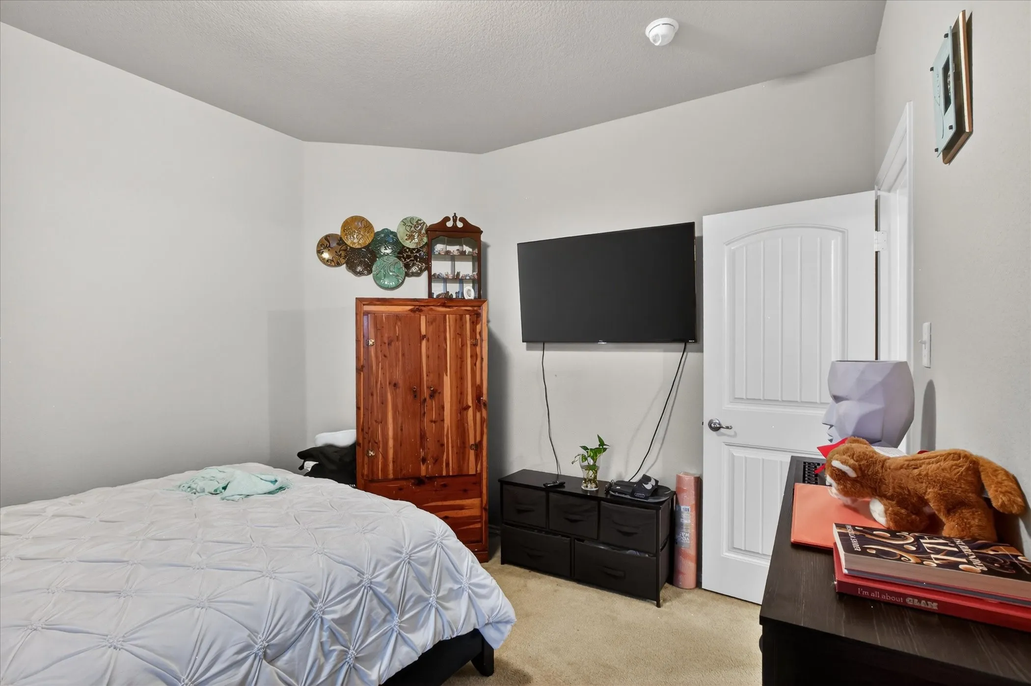 Bedroom featuring light neutral wall paint, white interior door with paneling, carpet flooring, and a ceiling-mounted smoke detector