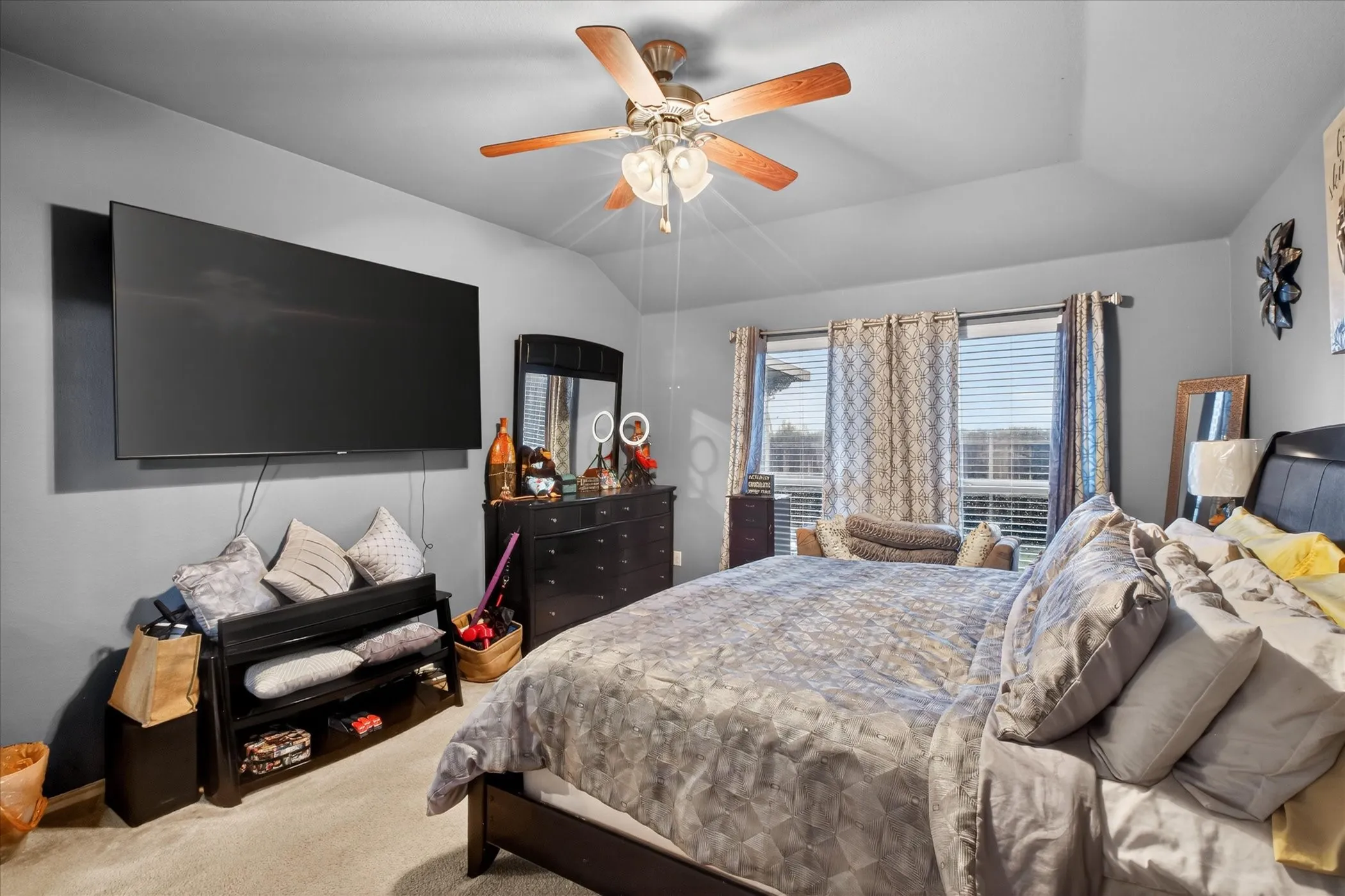 Spacious room featuring vaulted ceilings, a ceiling fan with integrated lighting, multiple windows providing natural light, and neutral wall-to-wall carpeting