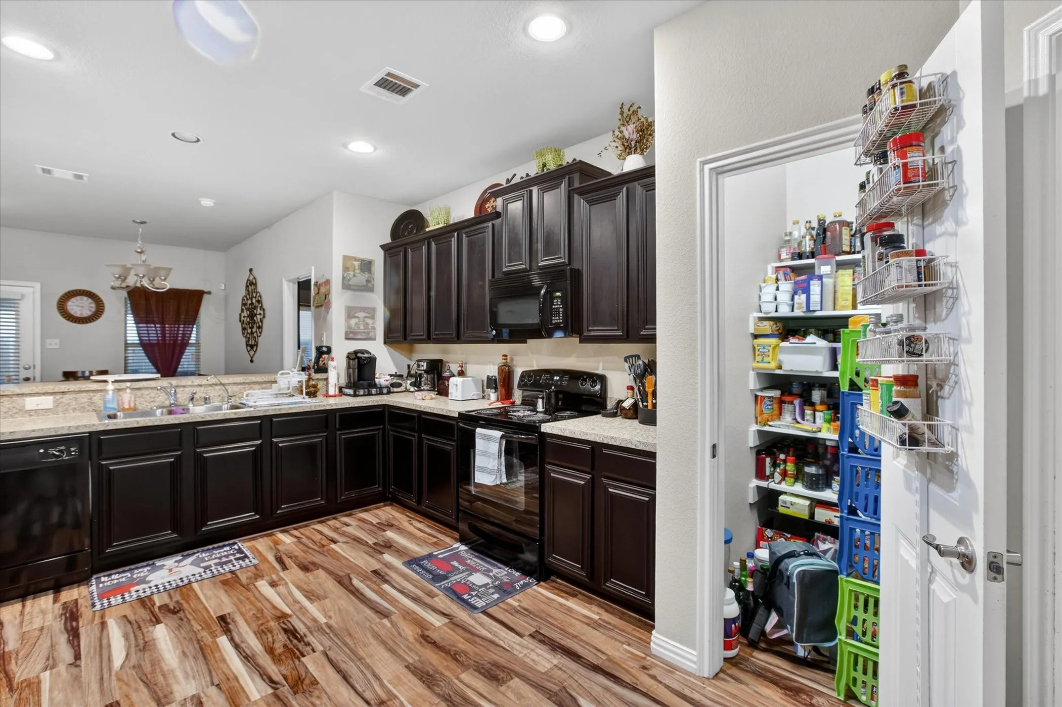 Kitchen featuring dark wood cabinetry, granite countertops, black appliances, and wood-finish flooring