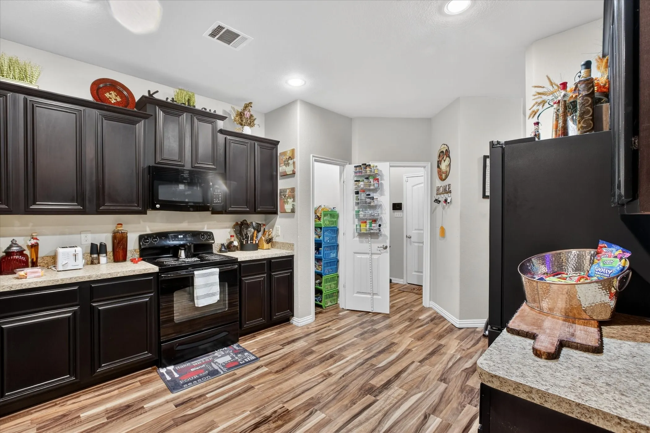 Kitchen featuring dark wood cabinetry, granite-style countertops, wood-finish flooring, a black range with an over-the-range microwave, and a black refrigerator