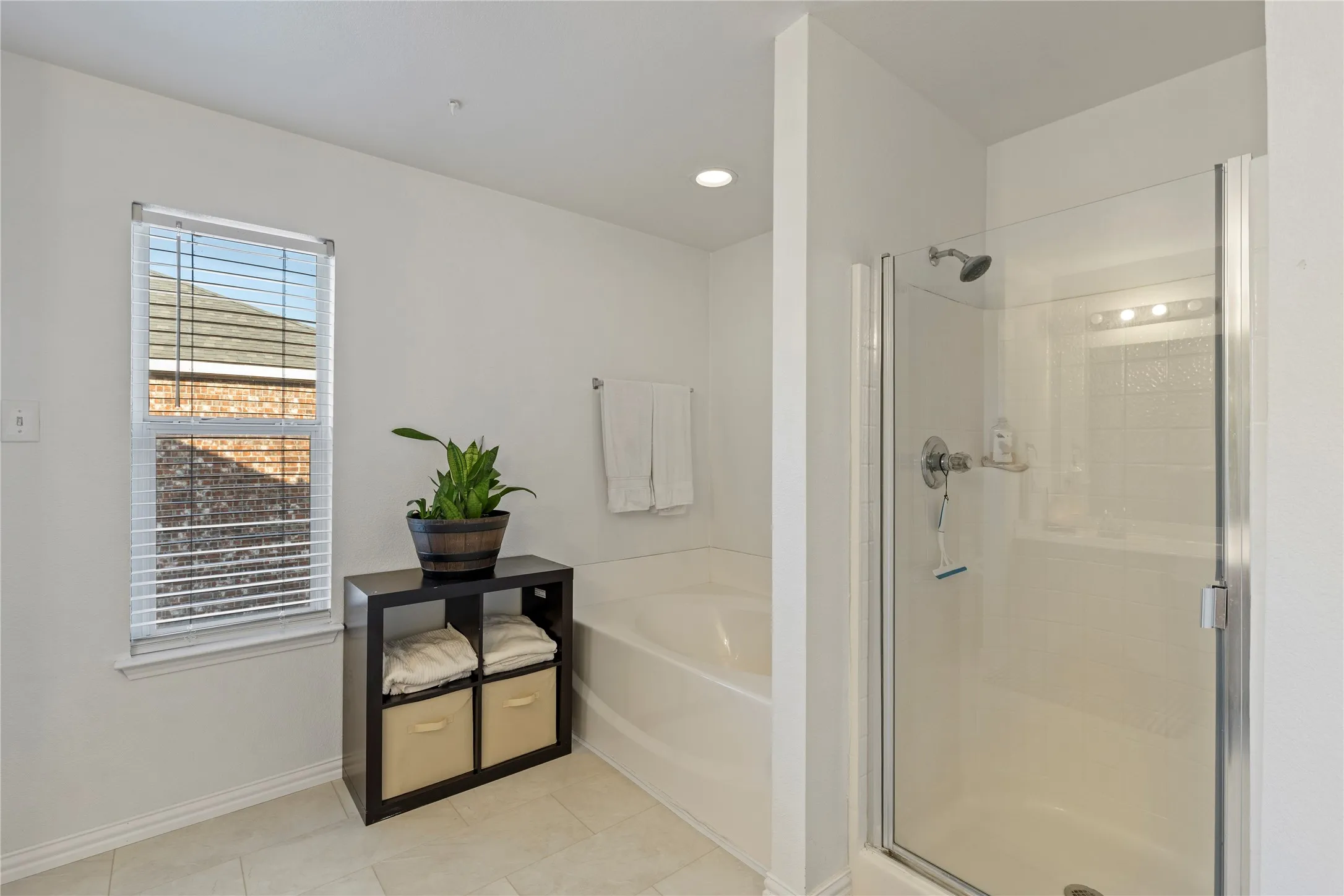 Bathroom featuring a glass-enclosed shower, a built-in soaking tub, a window with blinds, recessed lighting, and large format floor tiling