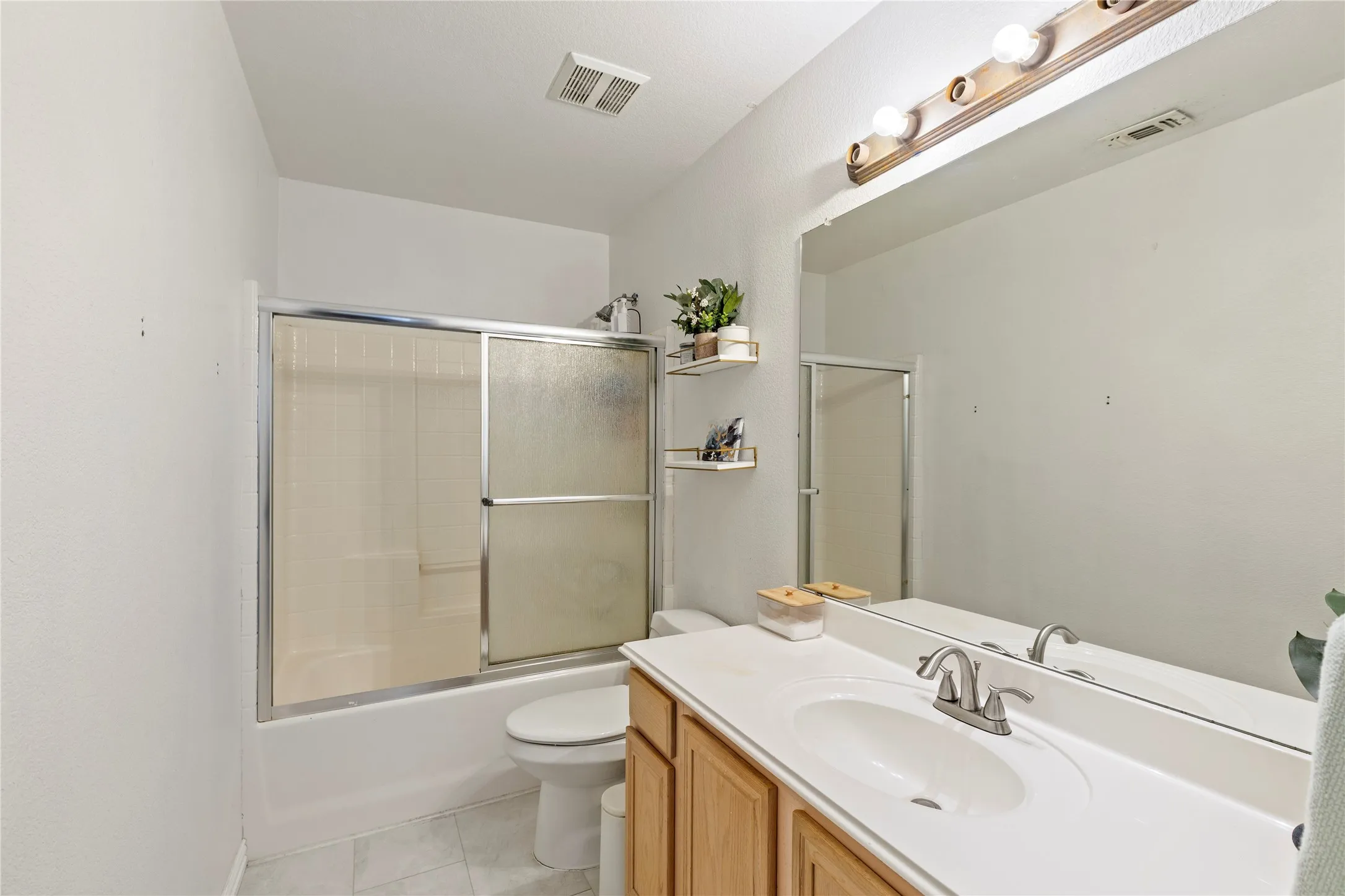 Full bathroom featuring a single vanity with a laminate countertop, chrome fixtures, a mirrored wall, and a combination tub and shower with sliding frosted glass doors