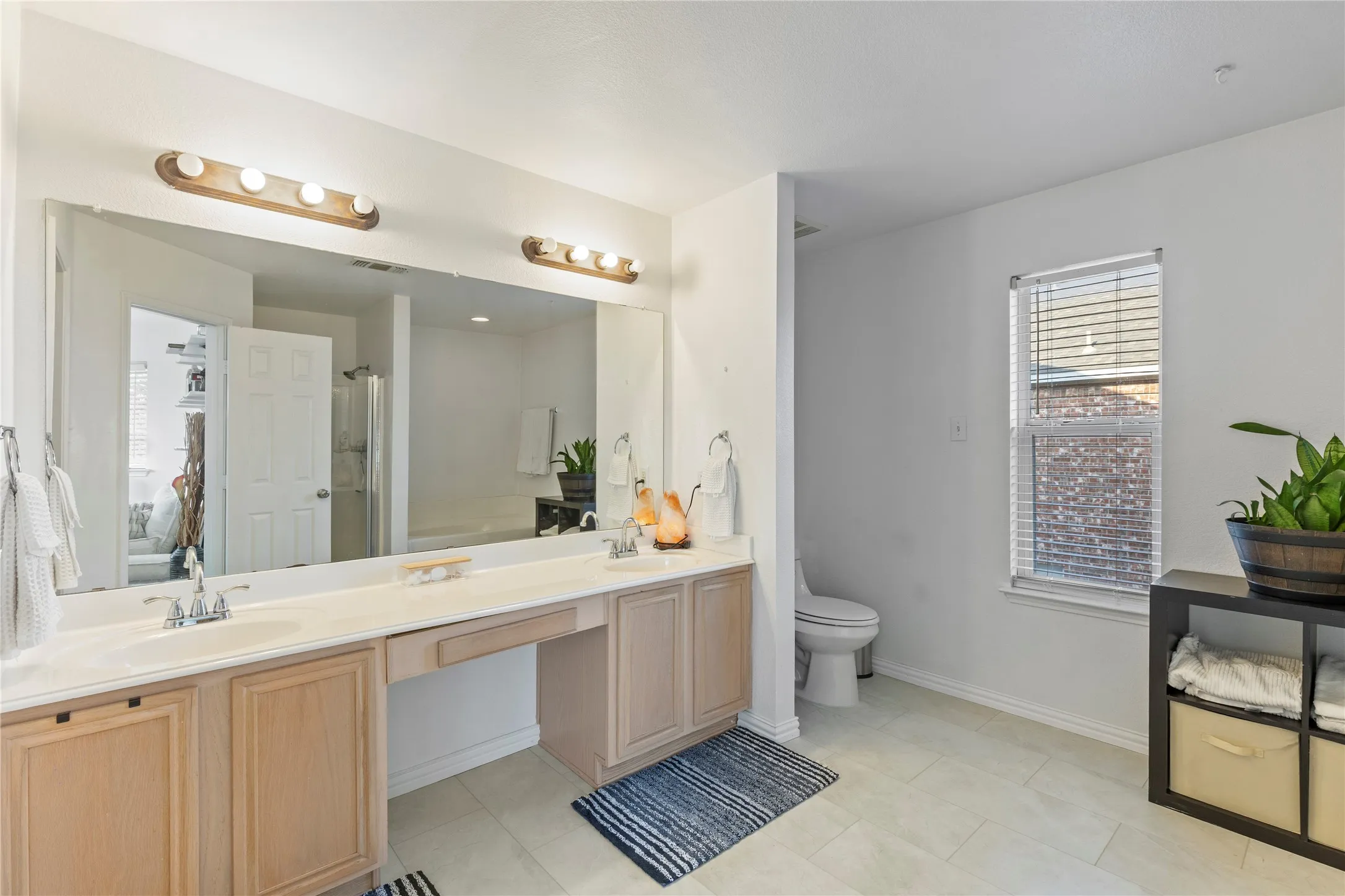 Bathroom featuring a dual vanity with light wood cabinetry, a built-in makeup area, and a large wall-mounted mirror