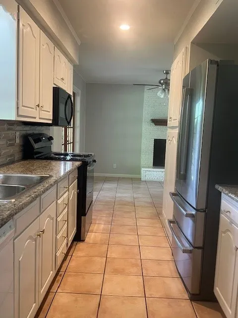 Kitchen featuring granite-style countertops, stainless steel refrigerator and range, tile flooring, and white cabinetry