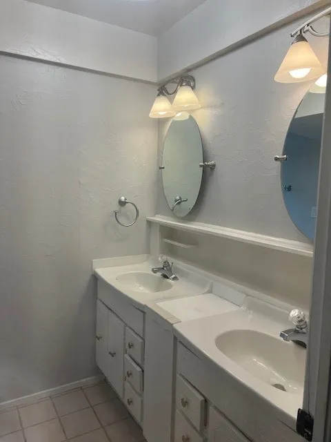 Dual vanity featuring white cabinetry, integrated sinks, chrome fixtures, and individual oval mirrors