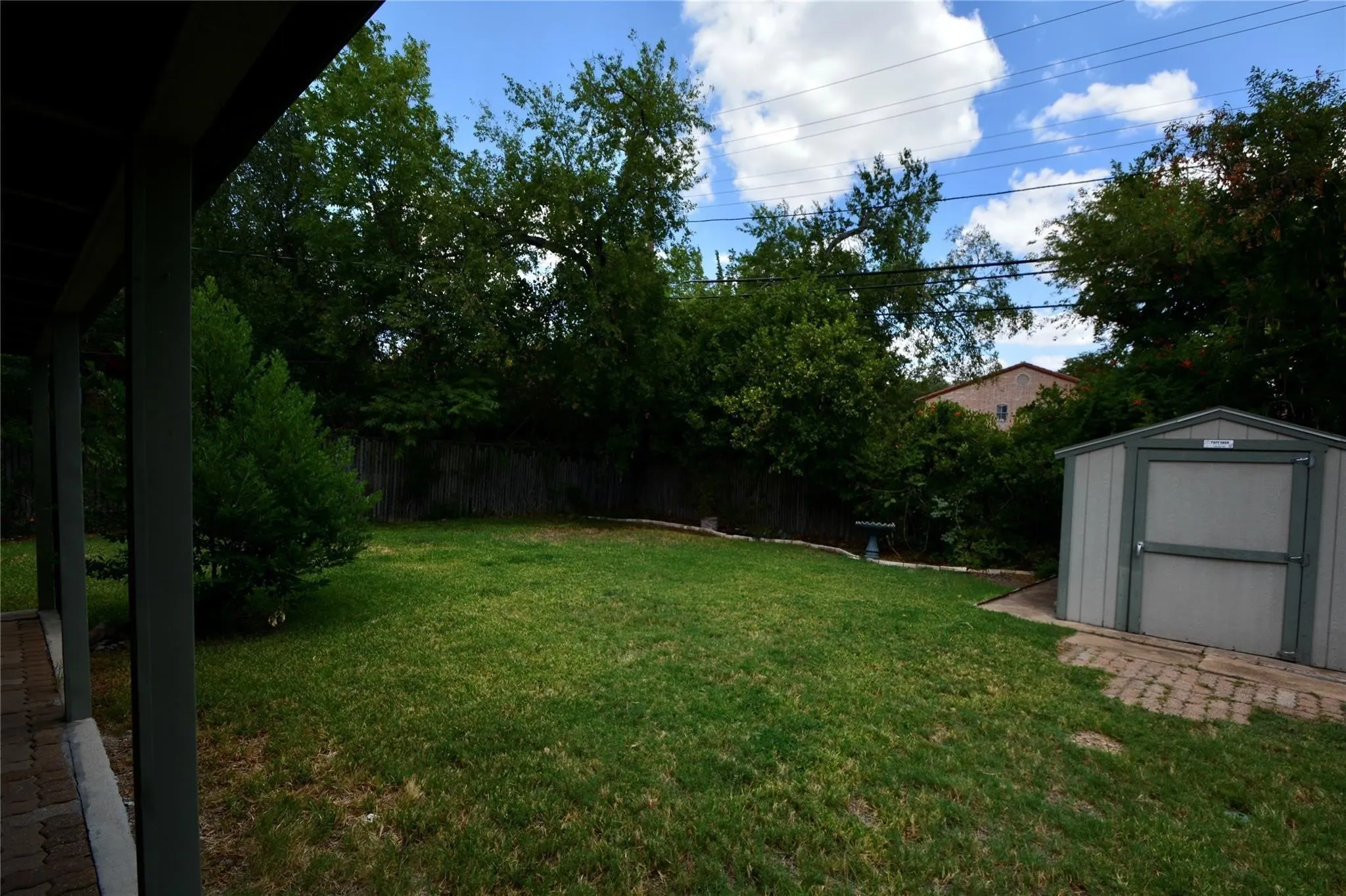 Spacious backyard featuring a manicured lawn, established trees, and a functional storage shed on a brick paver base