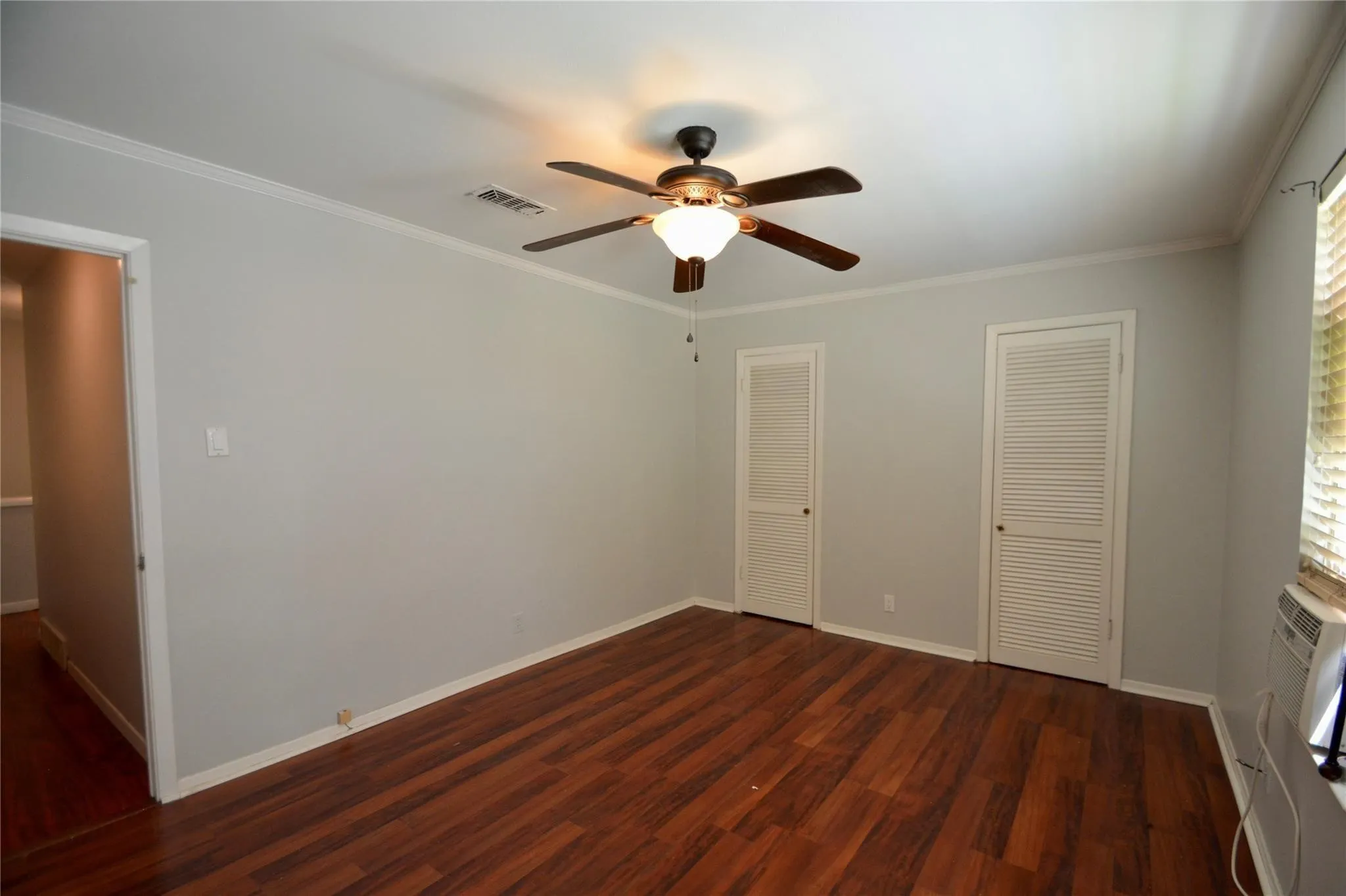Spacious room featuring wood-finish flooring, light gray walls, and white crown molding