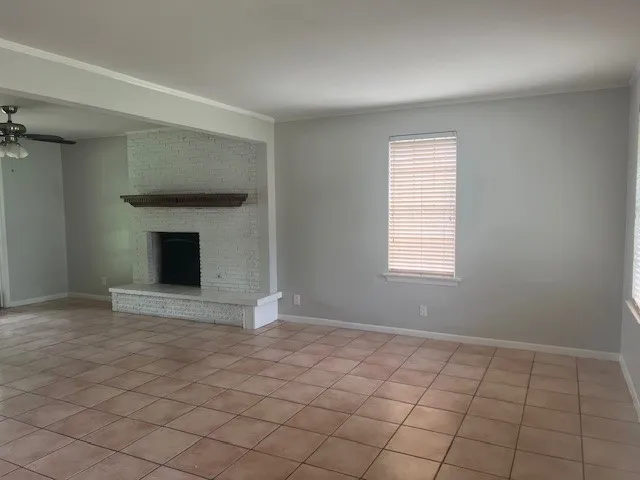 Spacious room featuring light-toned tile flooring, a white brick fireplace with a dark wood-finish mantel, and neutral gray walls