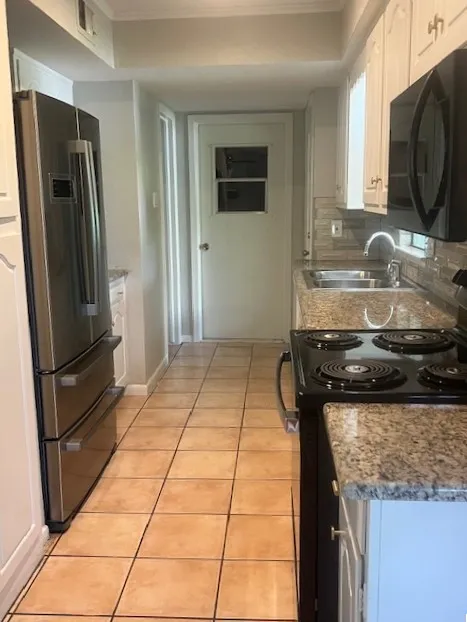 Galley kitchen featuring a stainless steel refrigerator, tile flooring, stone countertops, a tile backsplash, and white cabinetry