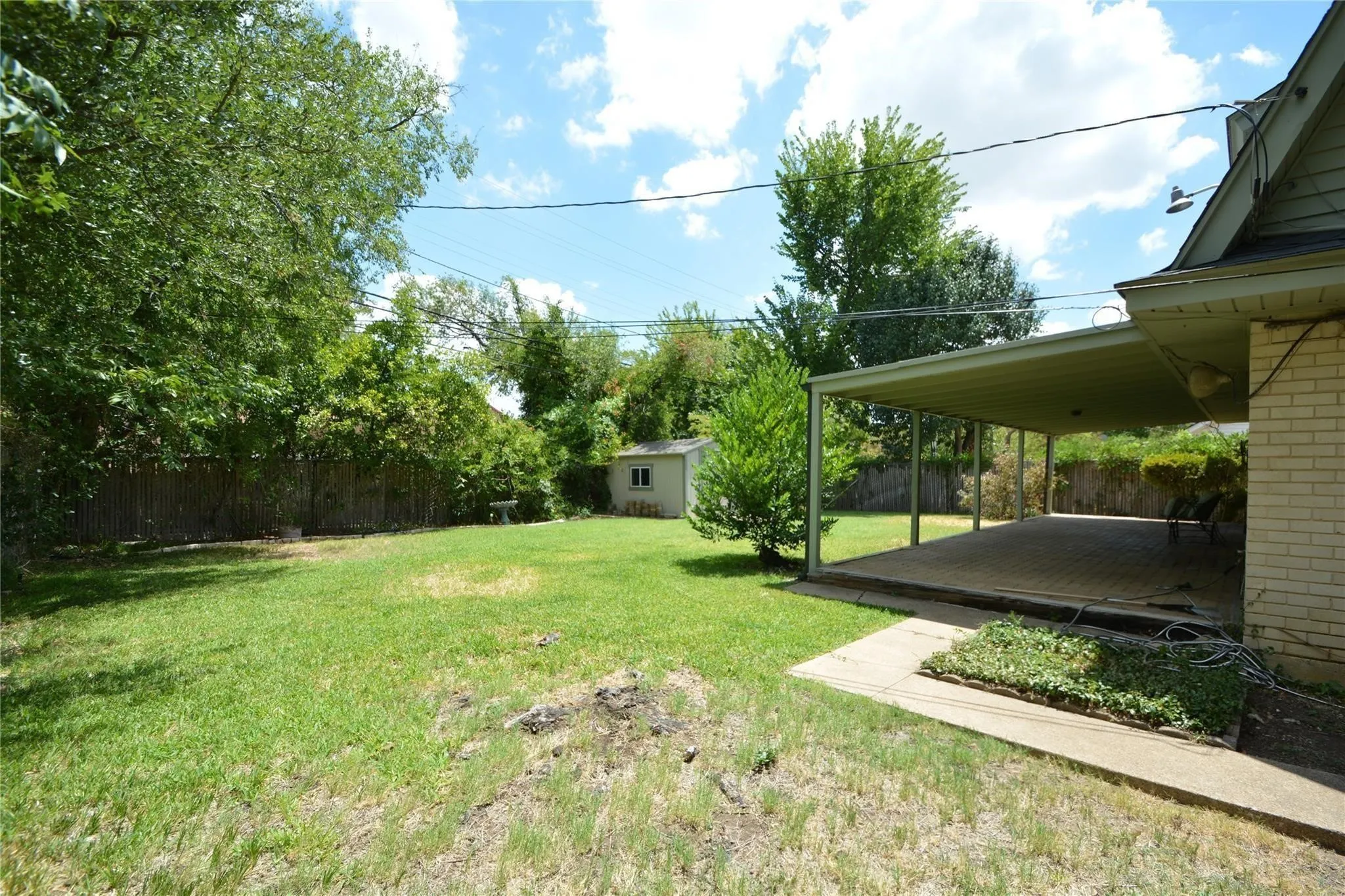 Expansive backyard featuring a covered patio, a separate storage shed, mature trees, and a wooden perimeter fence