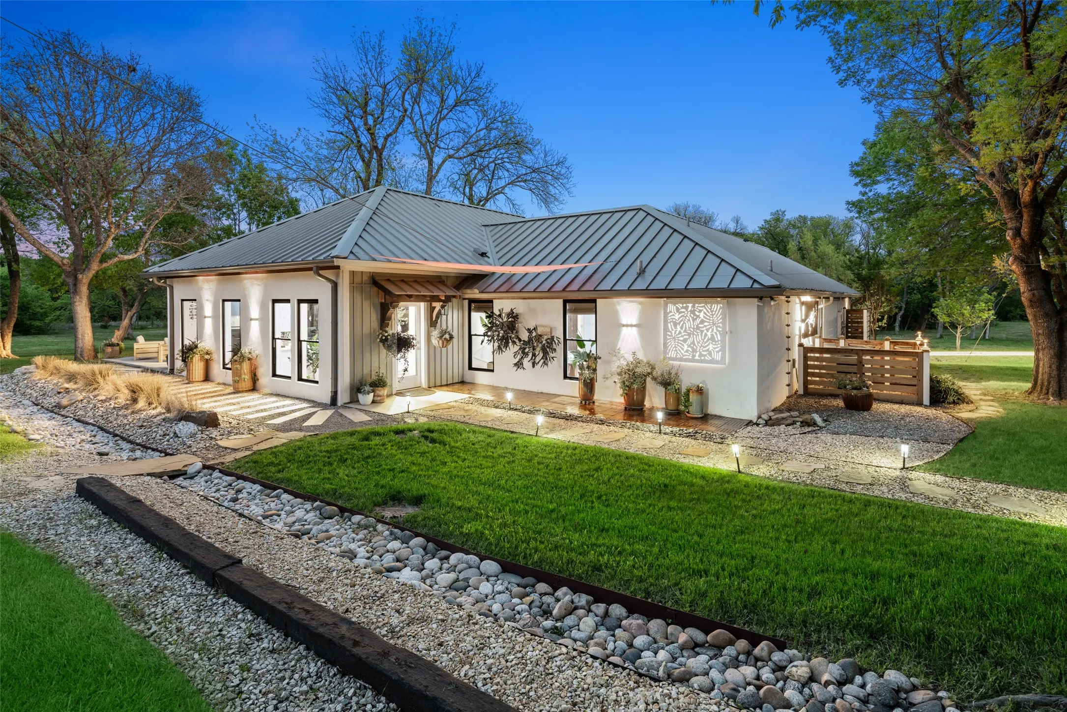 Back patio with designer landscaping leads to fenced corral and stables