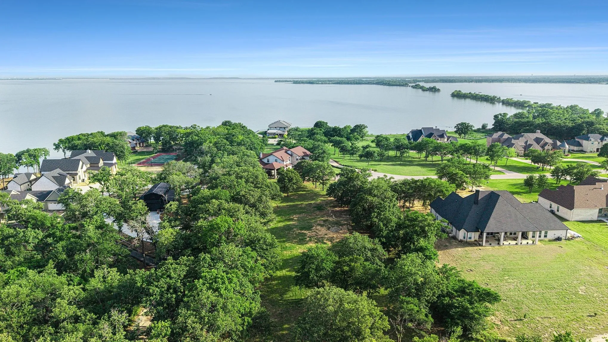 Sweeping waterfront aerial of Lake Lewisville’s shoreline with mature trees and nearby estate homes.