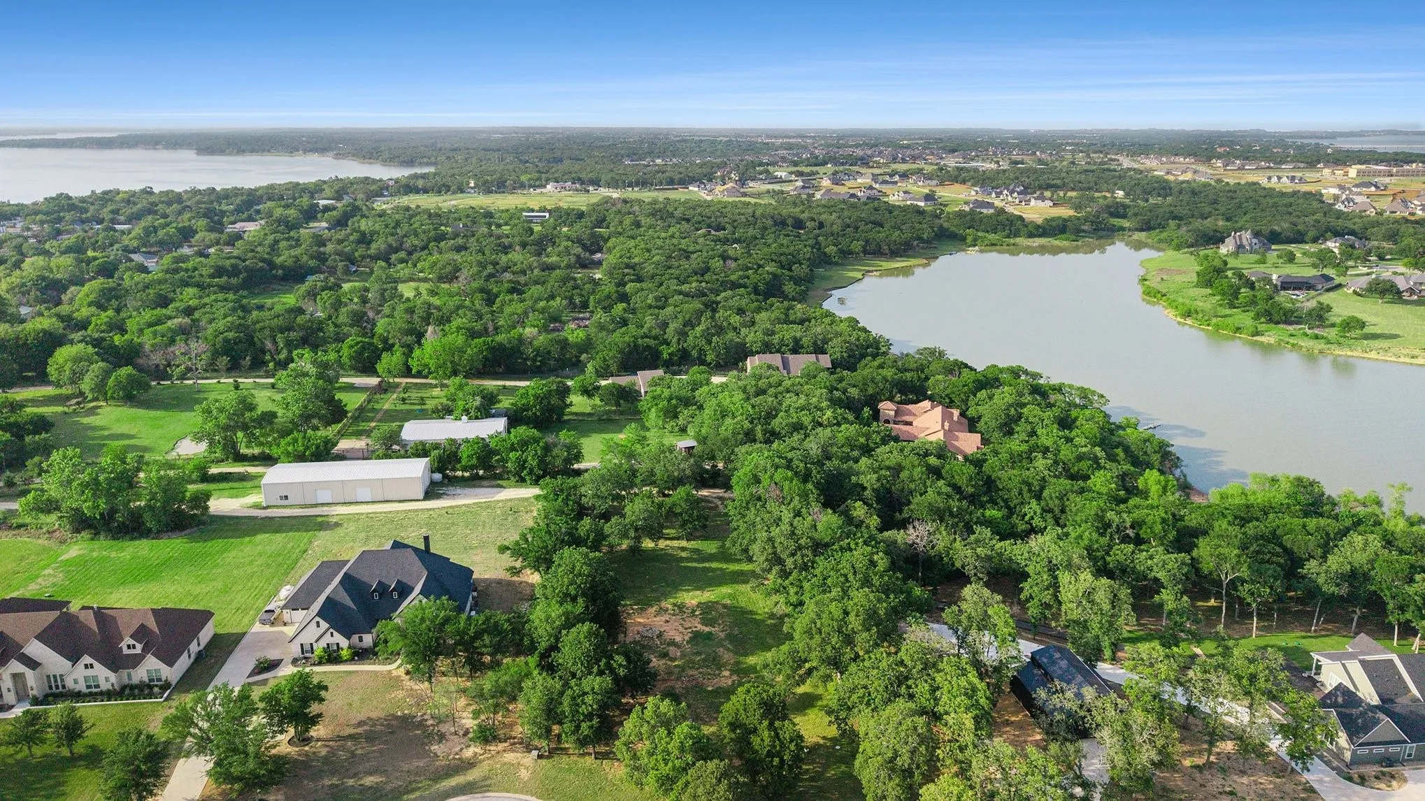 Aerial of the homesite approach with mature trees, paved drive, and surrounding estate residences.