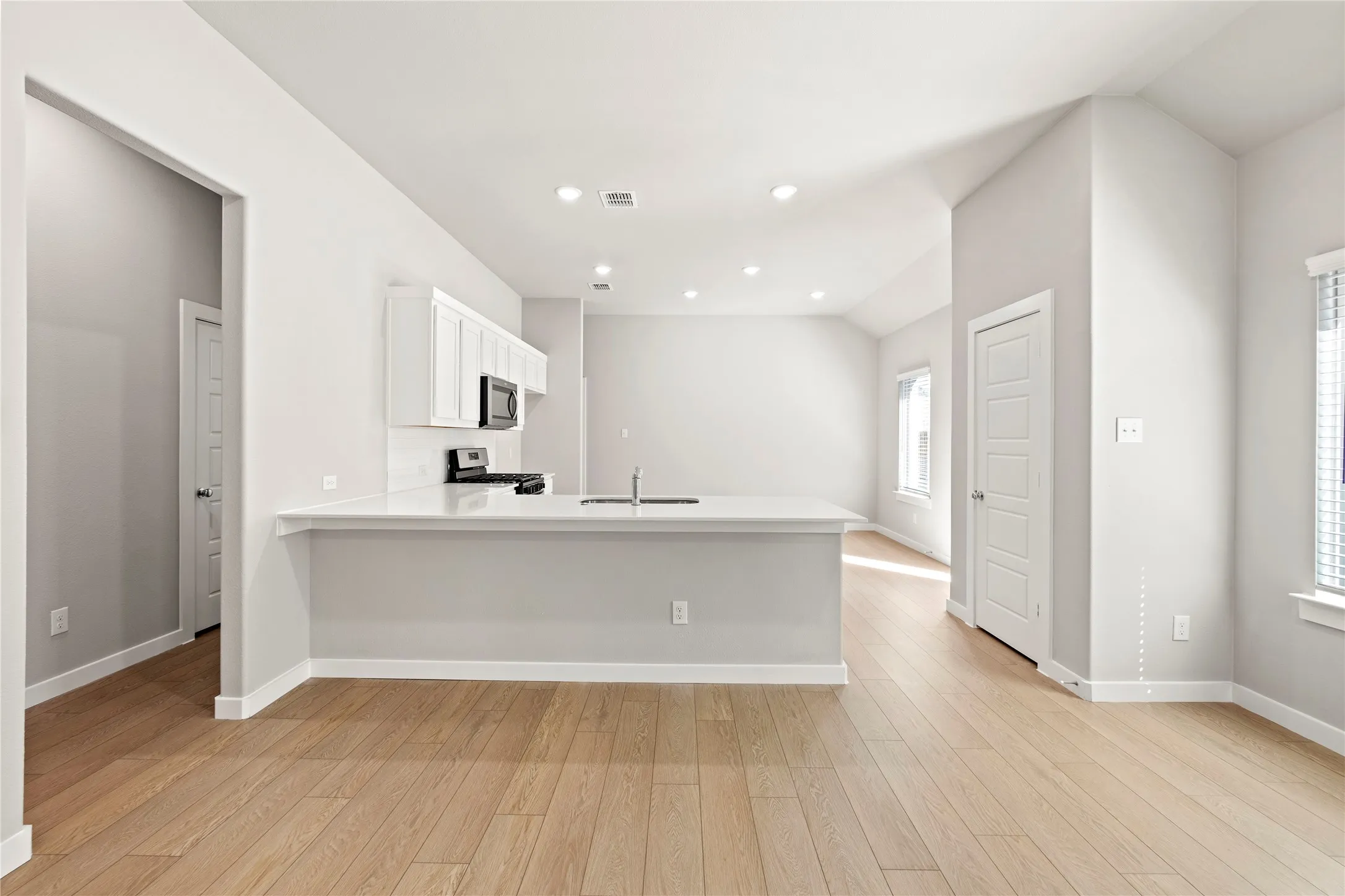Kitchen featuring white cabinets, light hardwood / wood-style flooring, stainless steel appliances, and vaulted ceiling