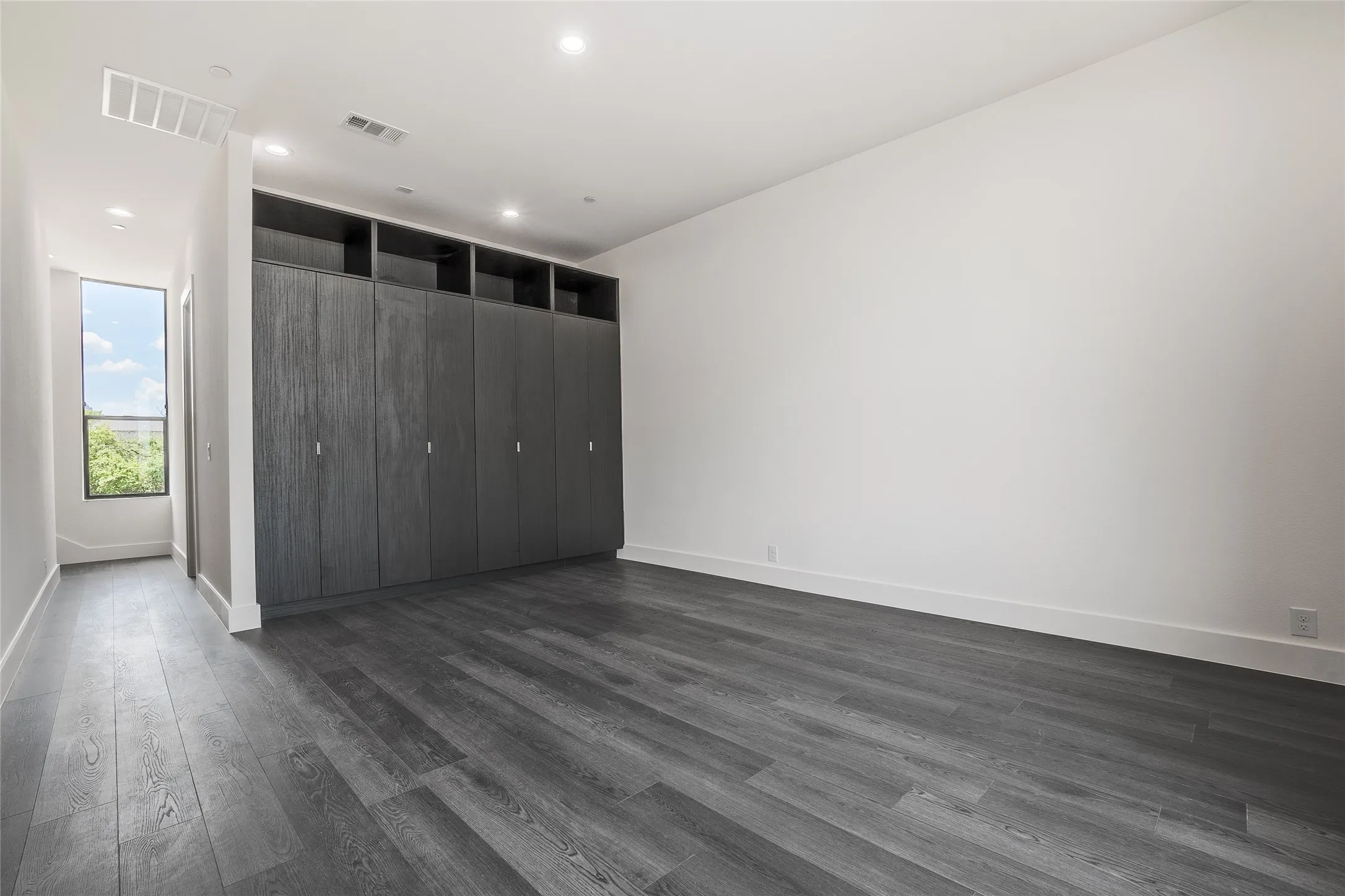 Spacious room featuring extensive built-in cabinetry with integrated shelving, dark wood-finish flooring, recessed lighting, and a large window
