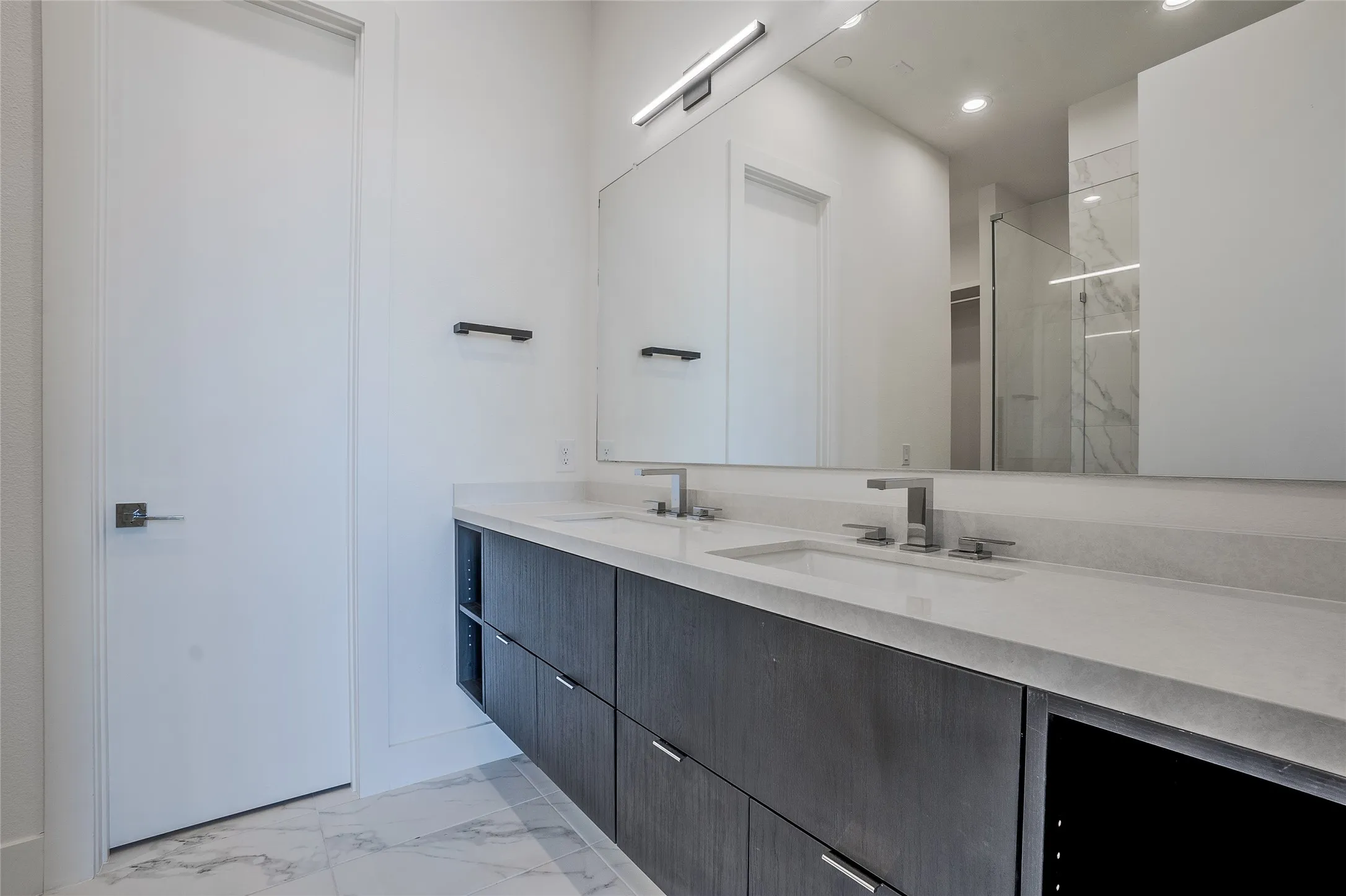 Dual sink vanity featuring a light-toned countertop, contemporary faucets, and dark wood-finish cabinetry