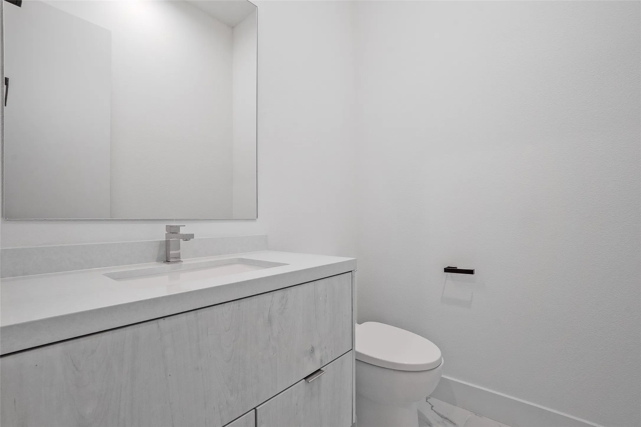 Bathroom featuring a floating vanity with a light wood-finish, an integrated sink with a brushed nickel faucet, a frameless wall mirror, and a white toilet