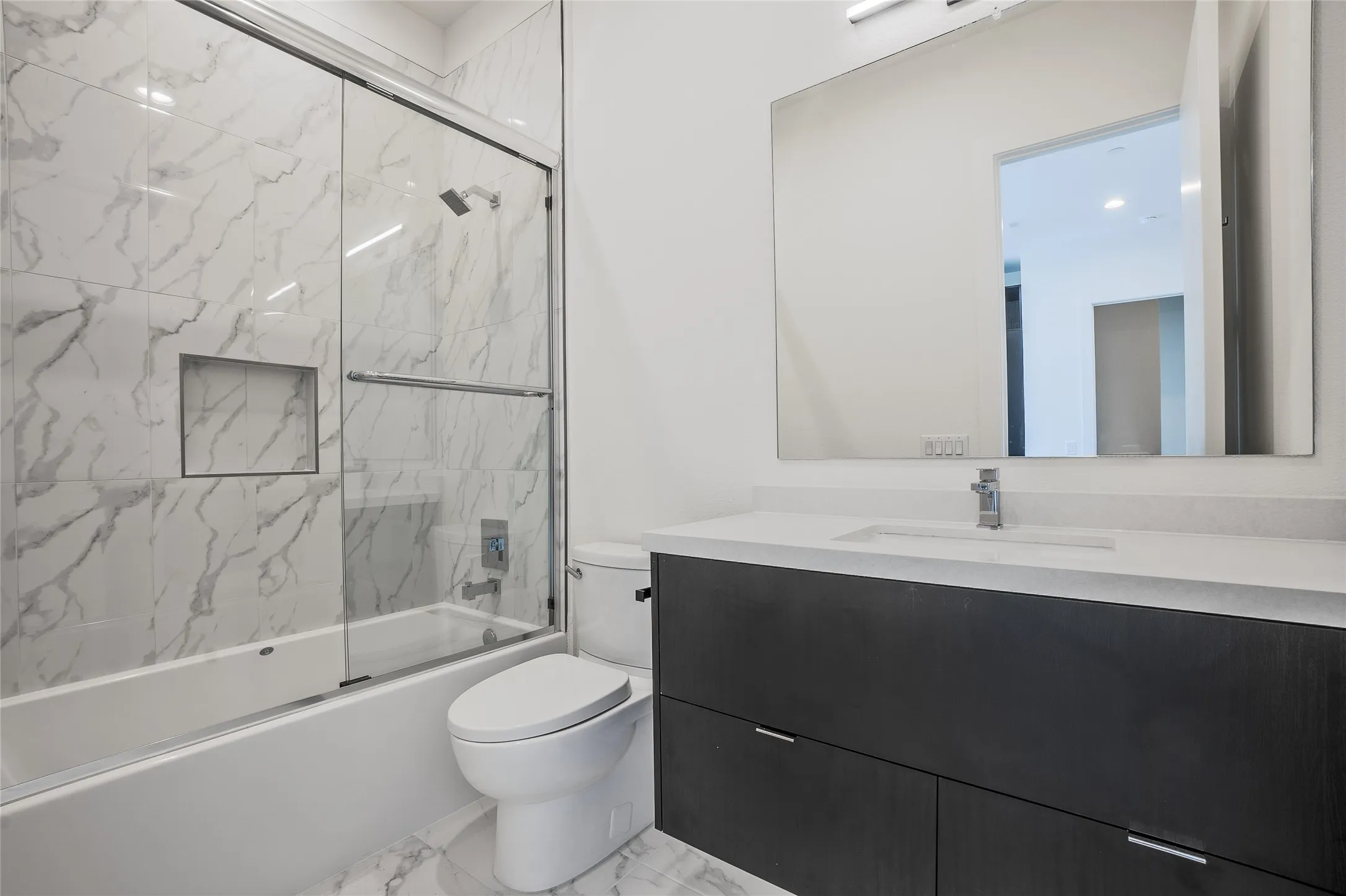 Bathroom featuring a soaking tub with sliding glass doors, white marble-style wall and floor tiling, and an integrated shower niche