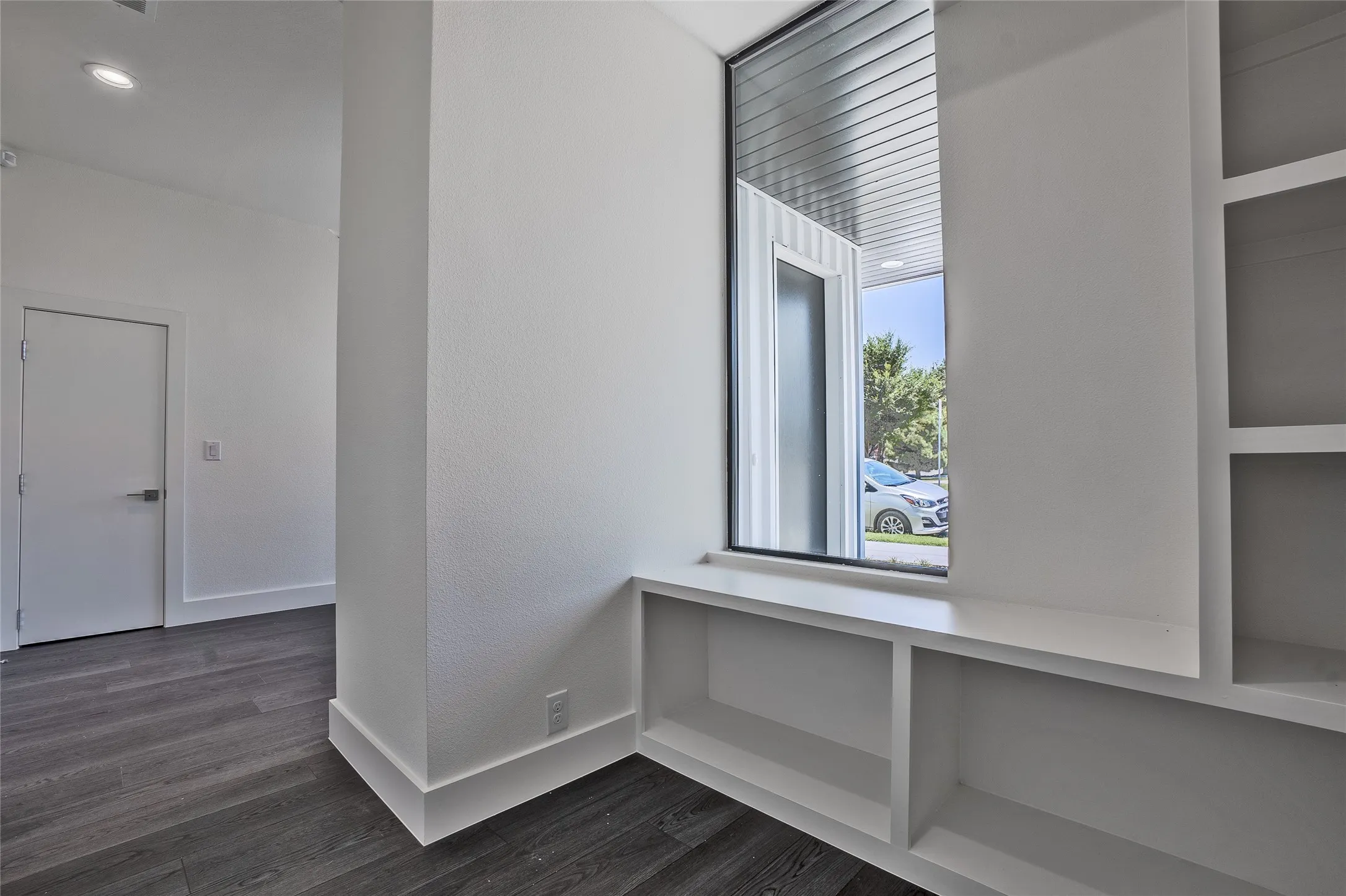 Built-in shelving and window bench with a large fixed window, recessed lighting, and dark wood-finish flooring