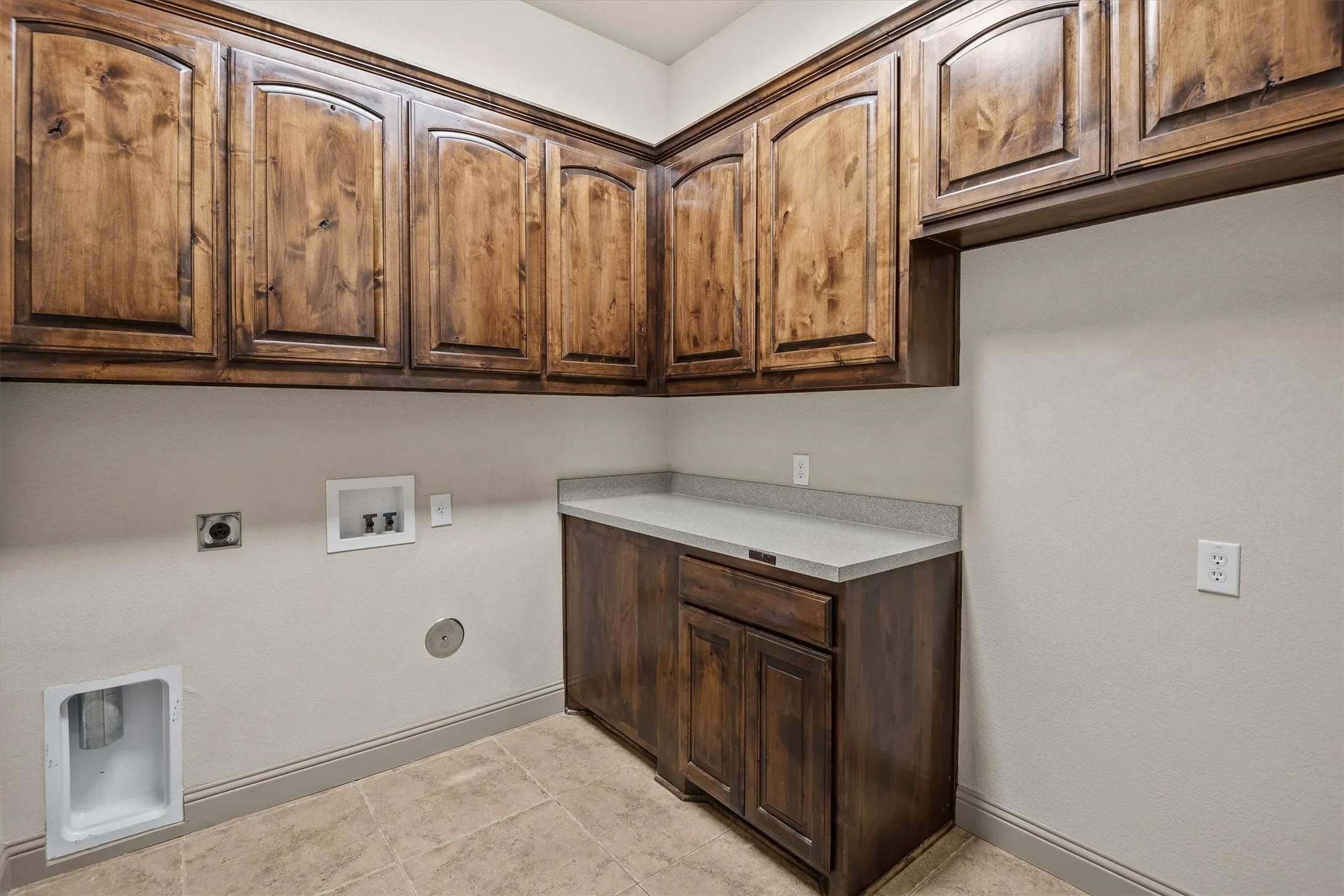 Utility area featuring ample dark wood cabinetry with arched details, a light-toned countertop, and durable tile flooring