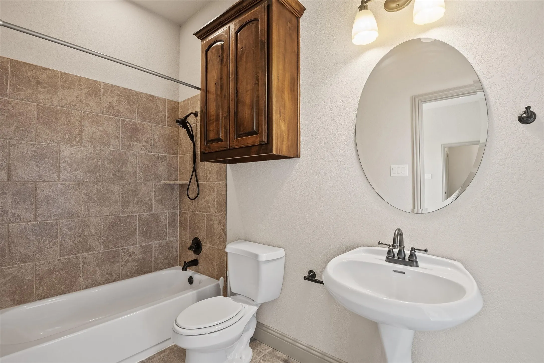 Bathroom featuring a white pedestal sink, an oval mirror, and a bronze-finish light fixture