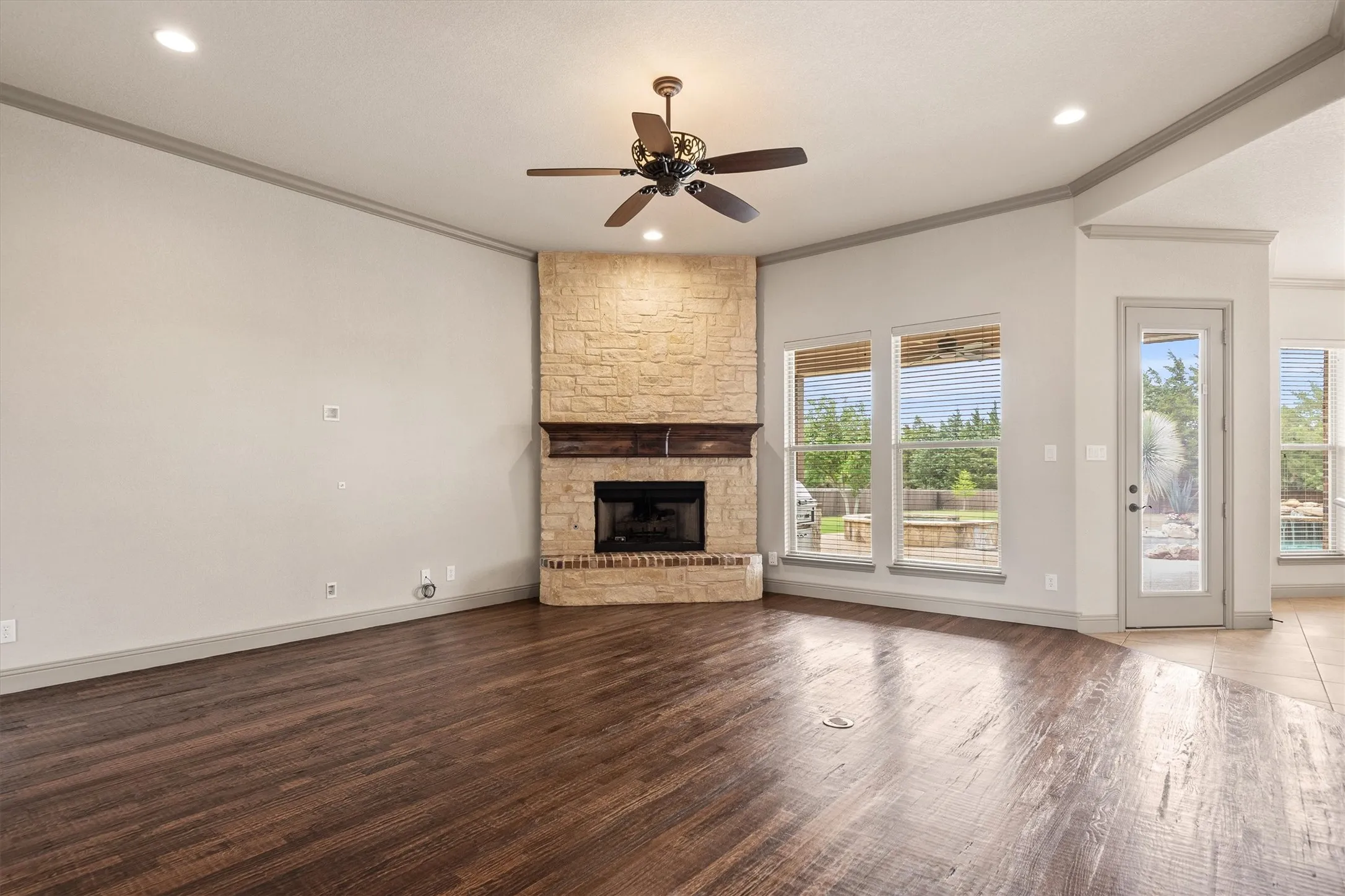 Corner stone fireplace with a wood mantle and dark wood-finish flooring