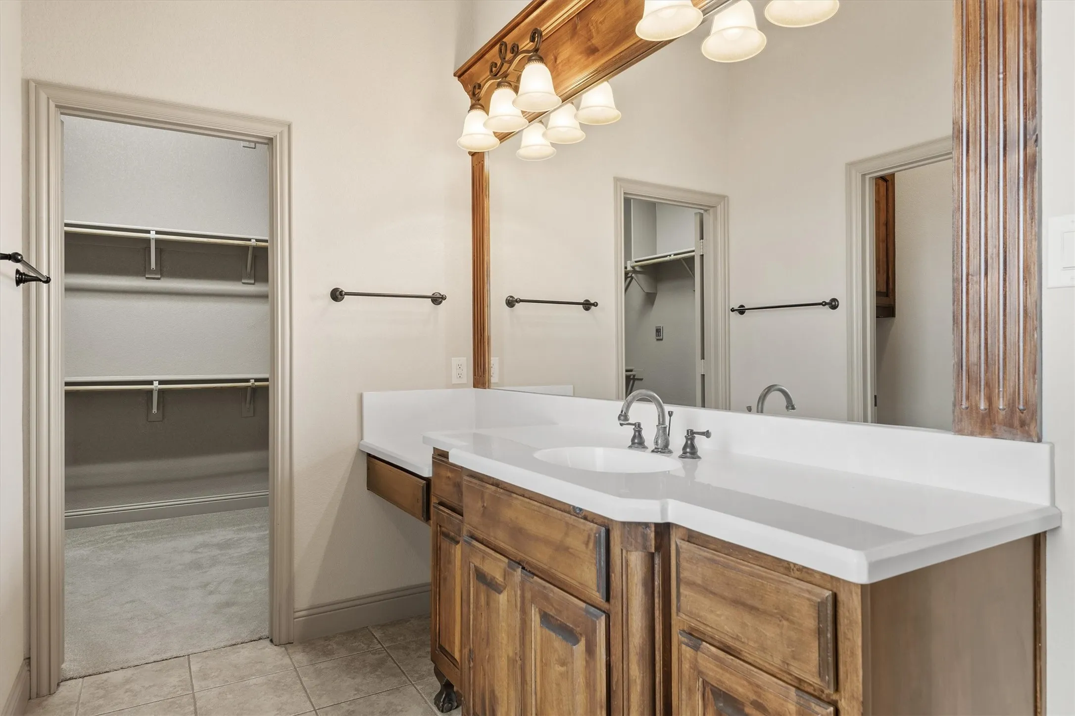 Bathroom vanity with a white countertop and integrated sink, complemented by a large mirror with decorative wood framing and an overhead light fixture