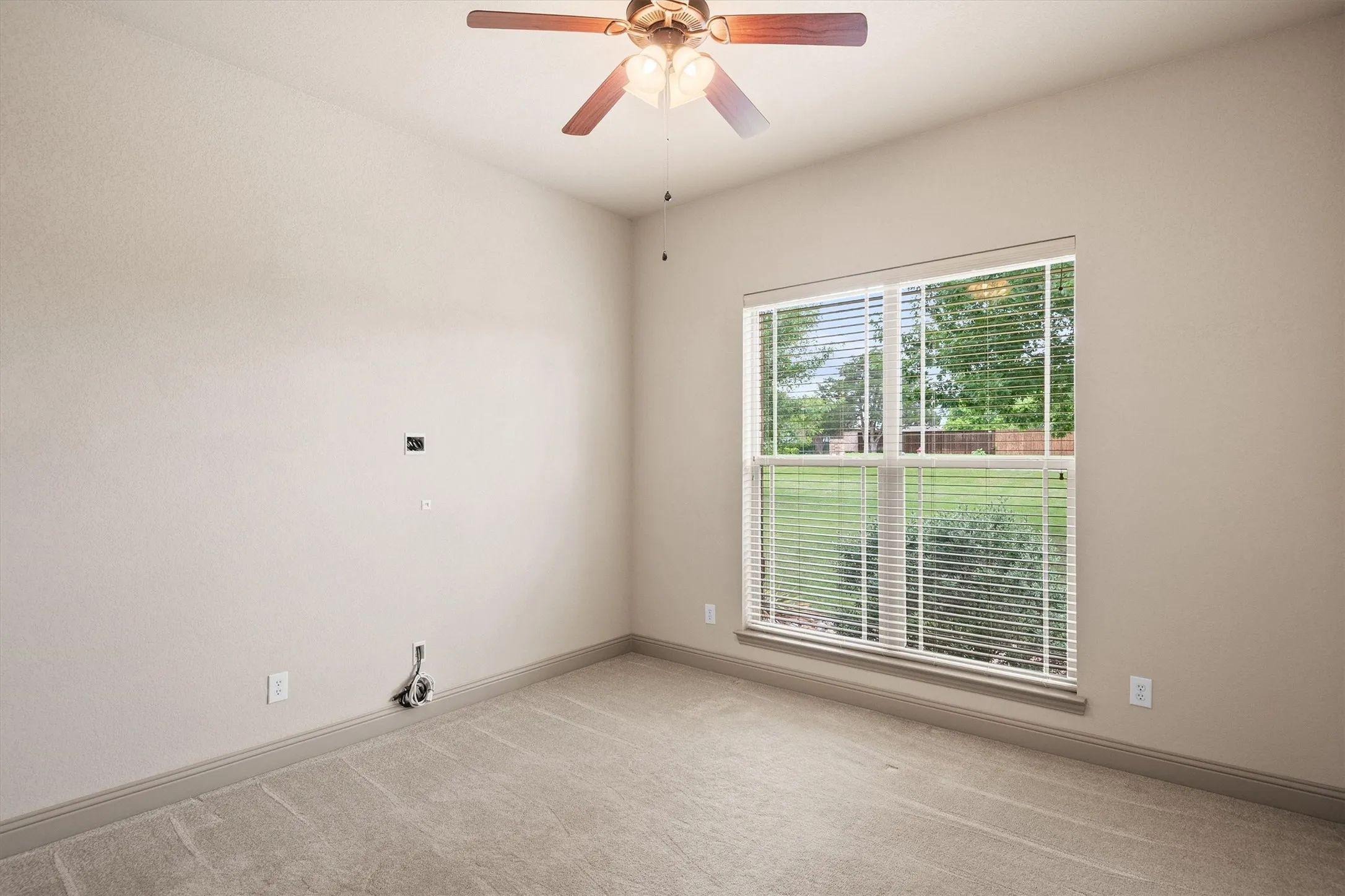 Carpeted room featuring a ceiling fan with light fixture, neutral wall color, and a large window with blinds