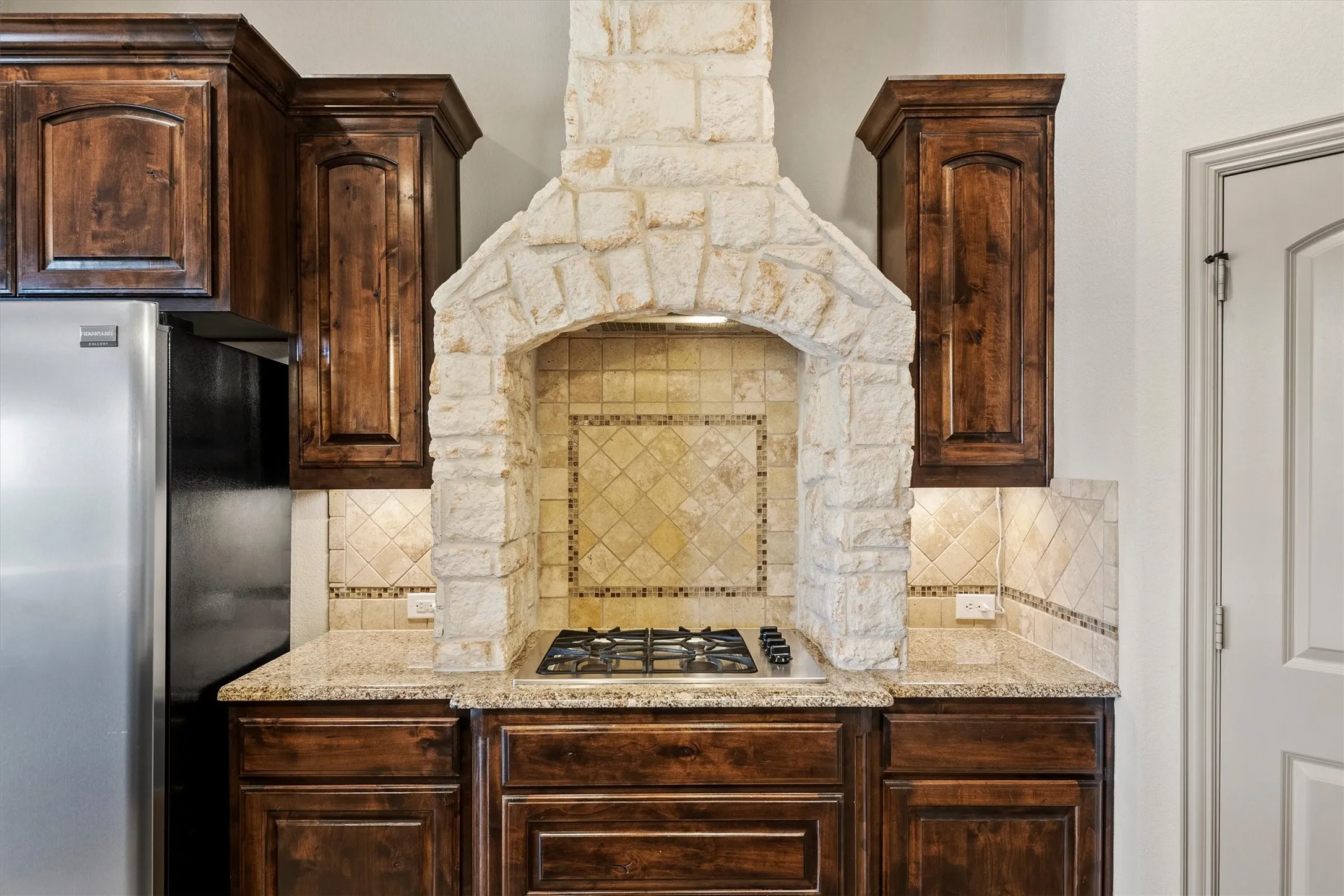 Kitchen featuring a stone-clad range hood over a gas cooktop, complemented by dark wood cabinetry and light-toned countertops
