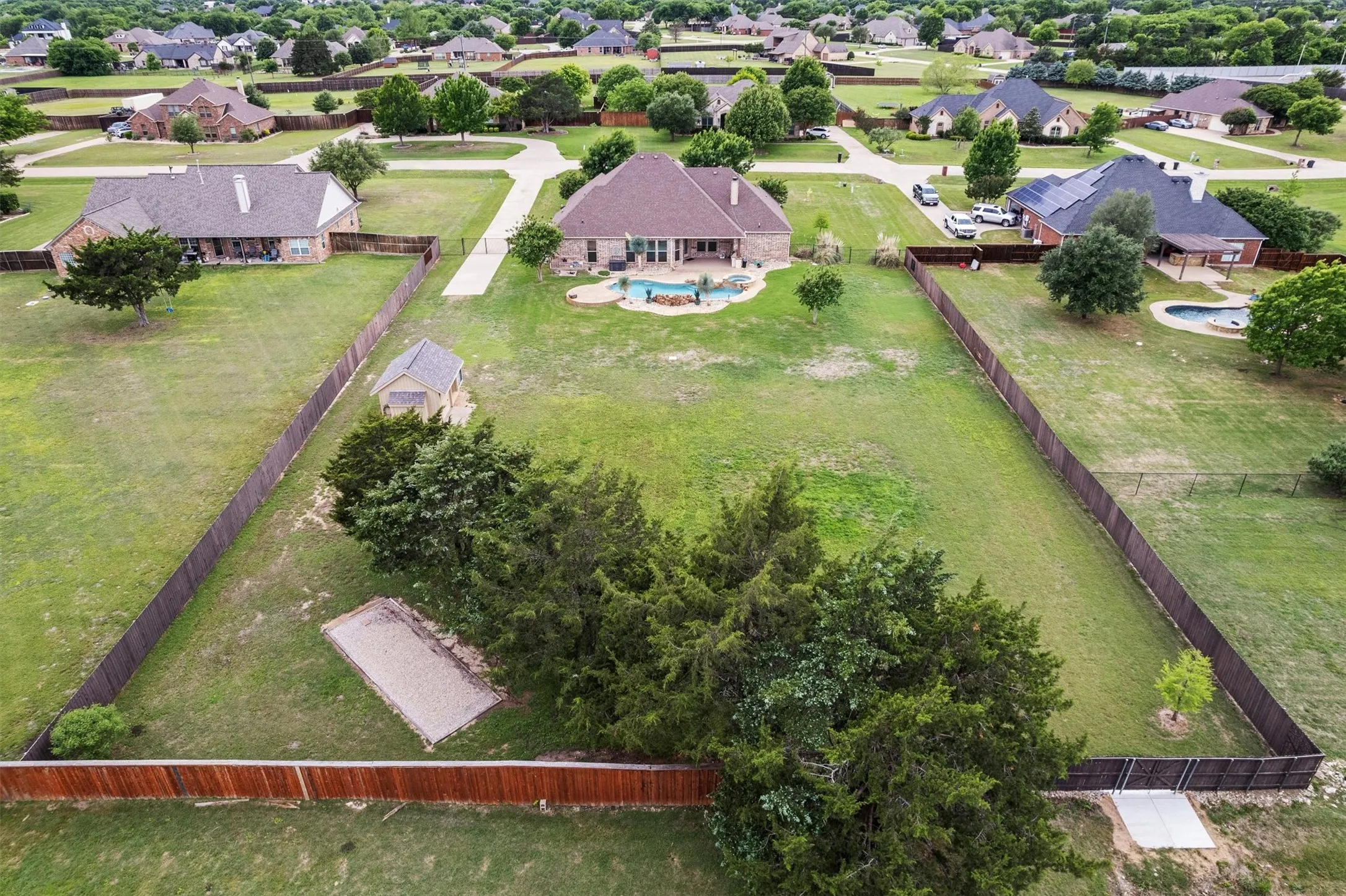 Expansive property featuring a brown shingle roof, a backyard swimming pool, a detached storage shed, a rectangular gravel area, and a wood fence enclosing the perimeter
