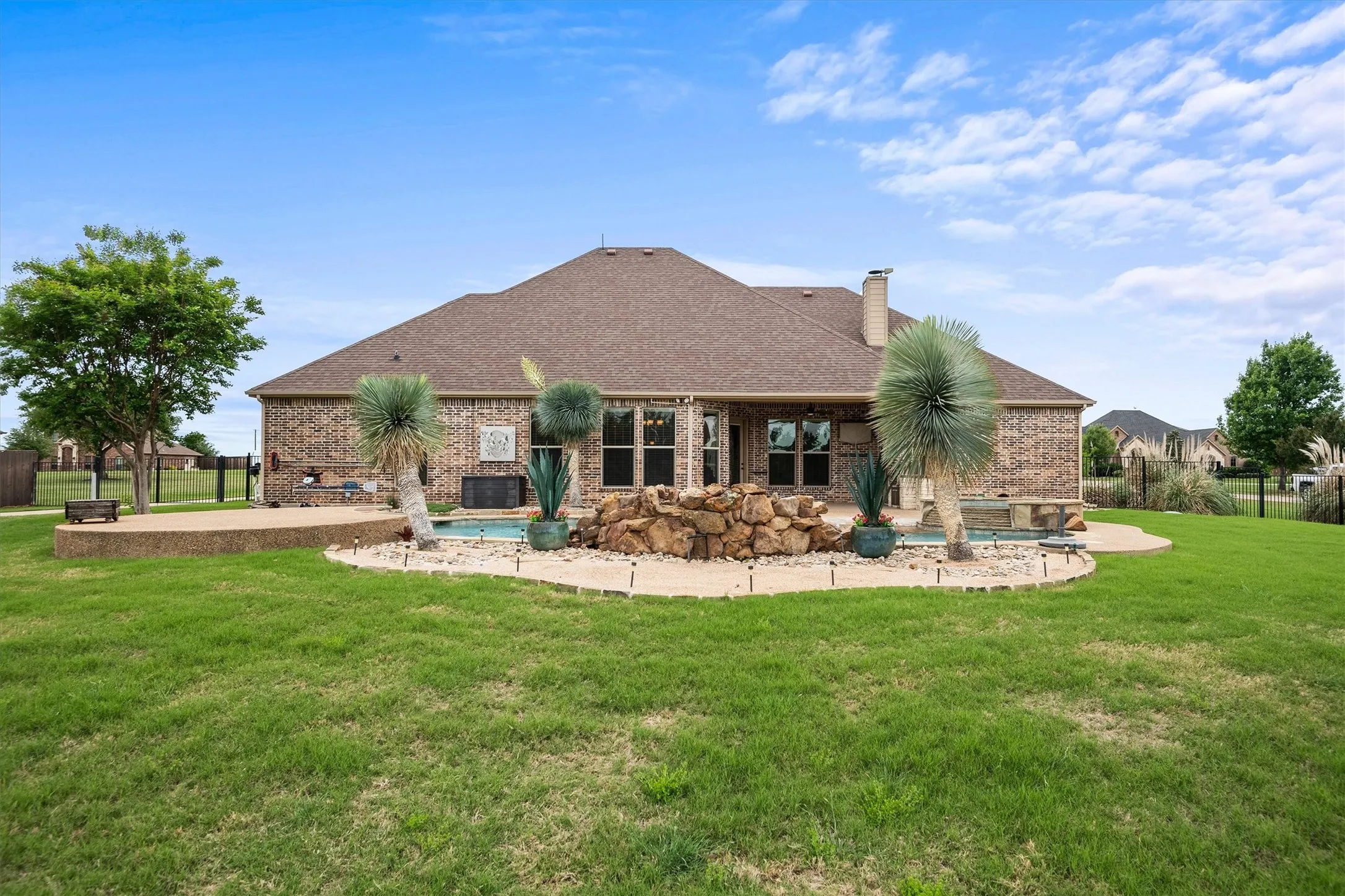 Expansive backyard featuring a swimming pool with a rock waterfall feature, an integrated patio area and a brick exterior