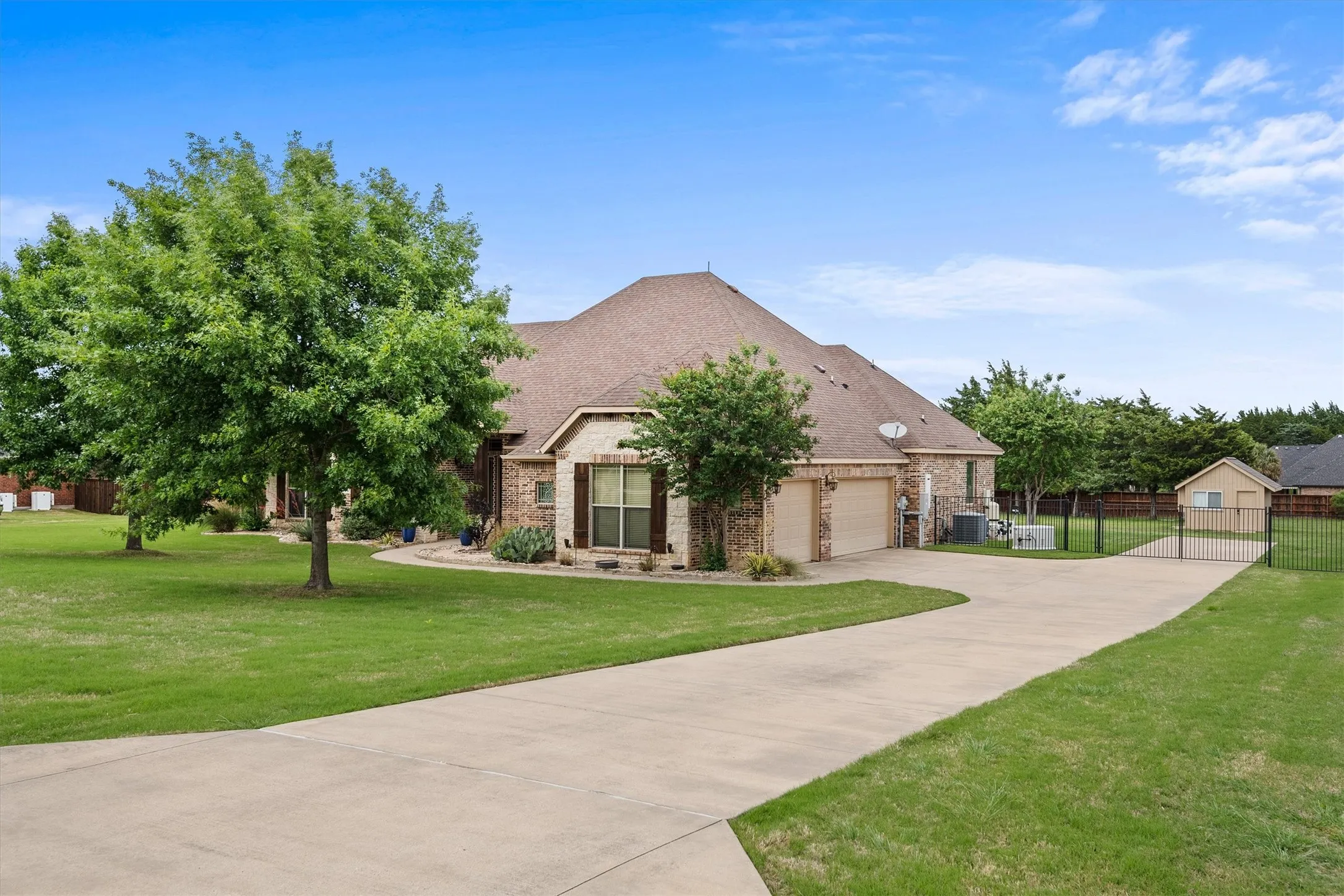Expansive concrete driveway leading to a brick and stone exterior residence with a three car garage