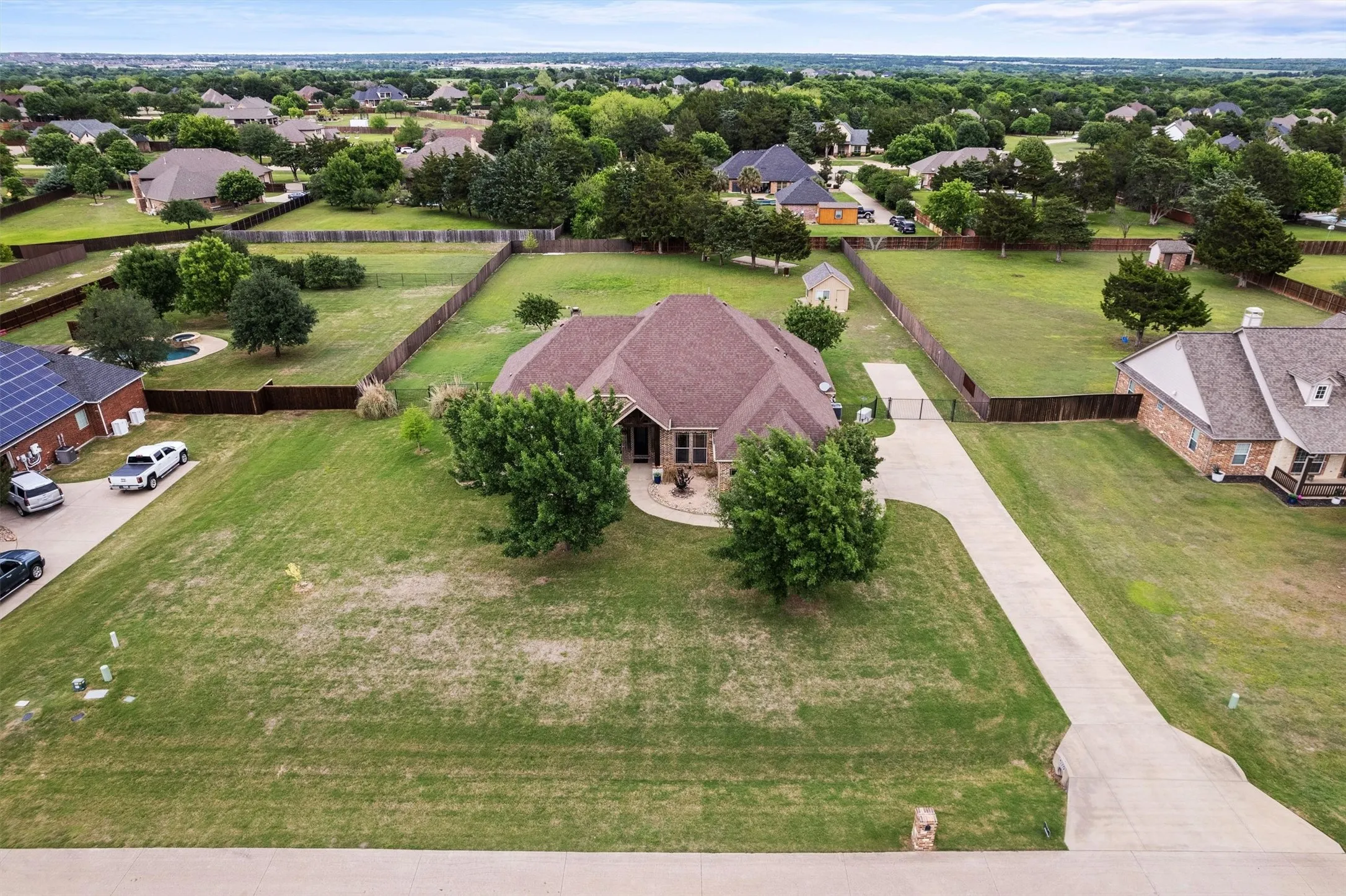 Spacious property featuring a single-story residence, extensive green lawn, mature trees, and a concrete driveway