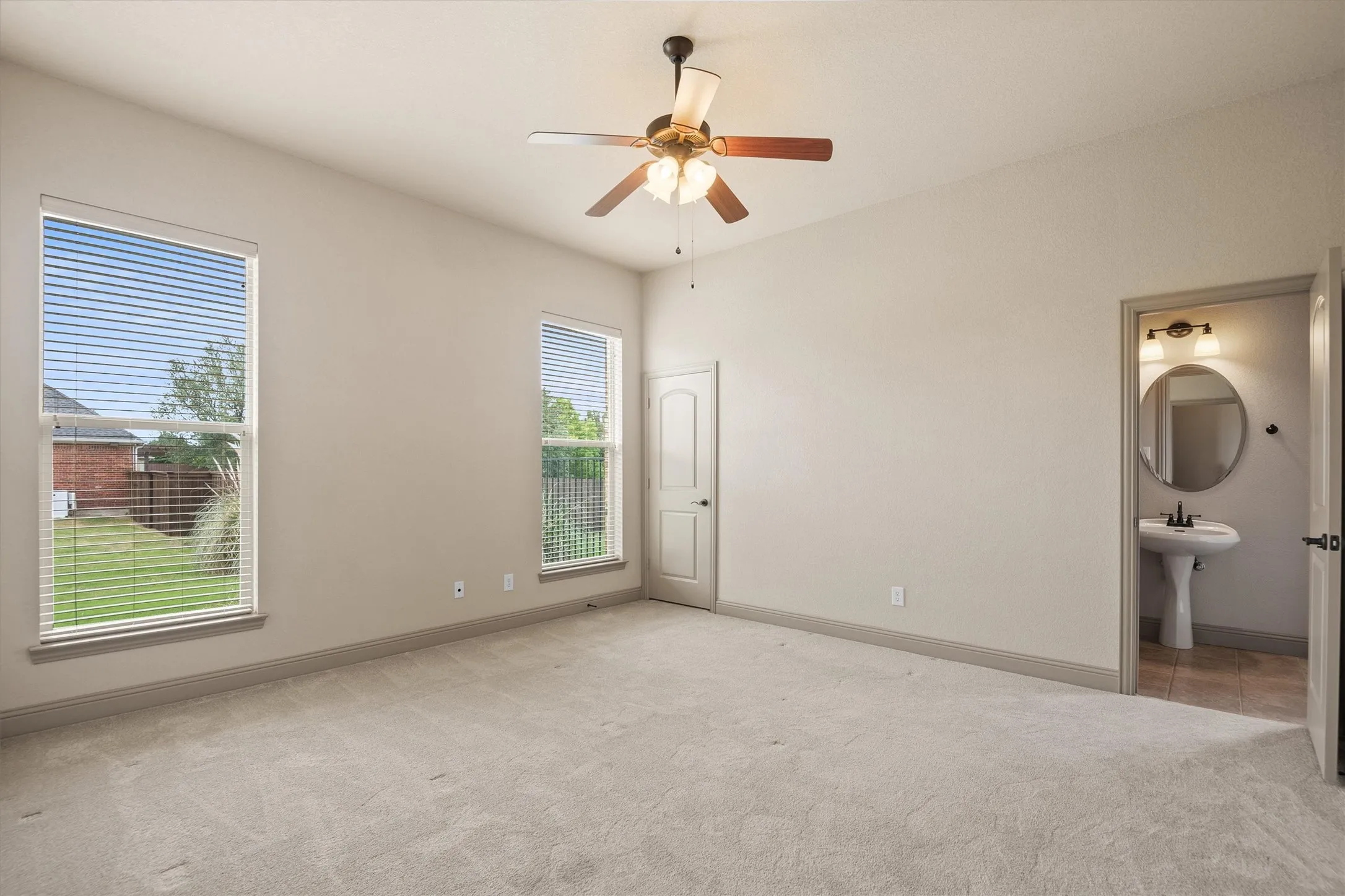 Spacious room featuring neutral carpeting, two large windows with blinds, and a ceiling fan with light fixture