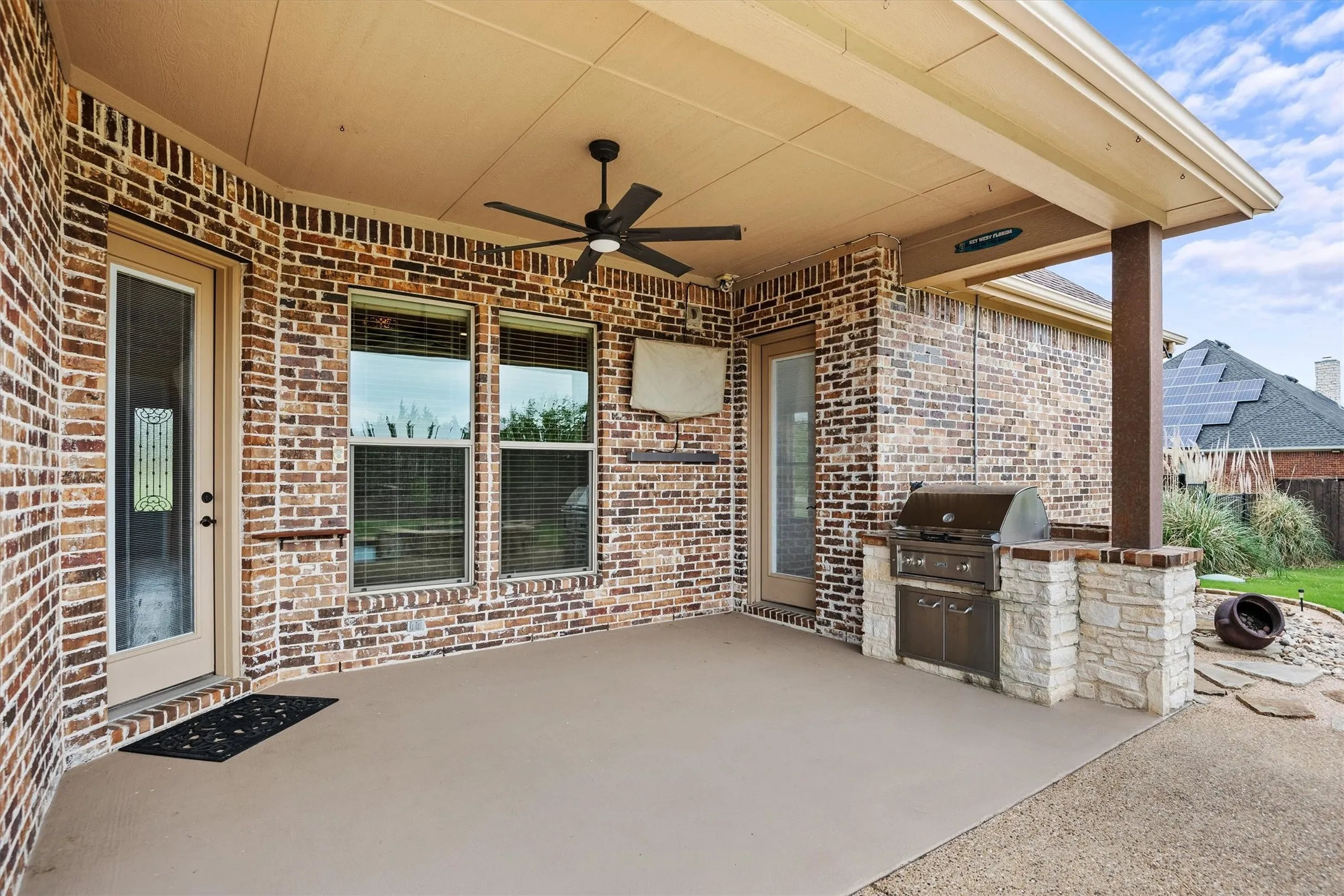 Covered patio featuring a built-in outdoor grill, a ceiling fan, and brick and stone accents