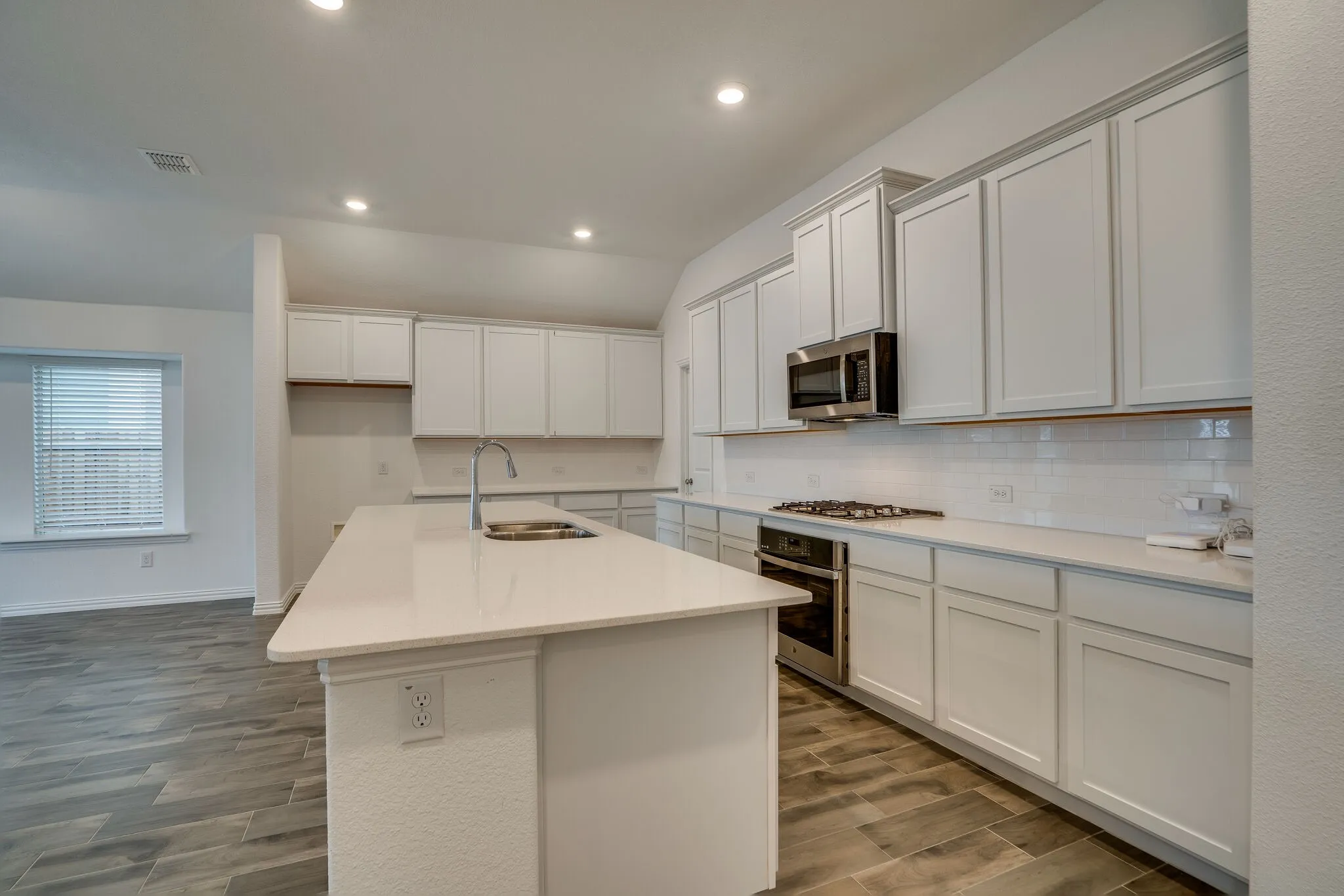 Modern kitchen featuring white shaker cabinetry, quartz countertops, a large island with an undermount sink, stainless steel appliances, and a subway tile backsplash