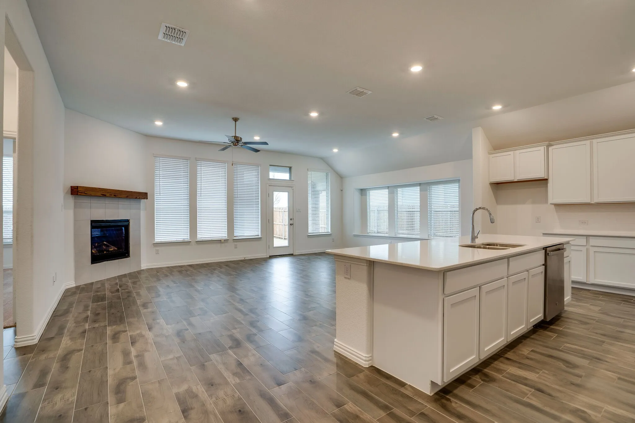 Open concept living area featuring wood-finish flooring, a contemporary fireplace with a rustic wood mantel, and multiple windows