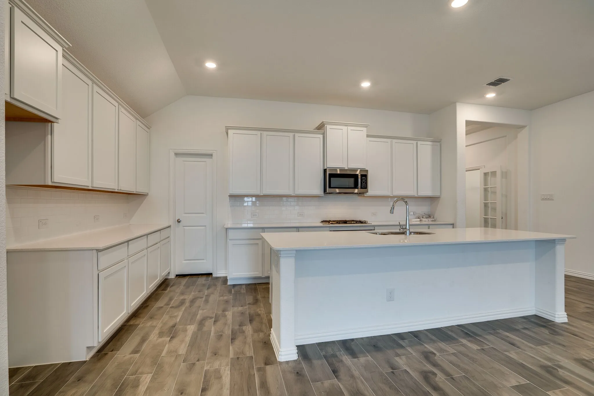 Spacious kitchen featuring an expansive island with an undermount sink, ample white cabinetry, a built-in microwave, and wood-finish flooring