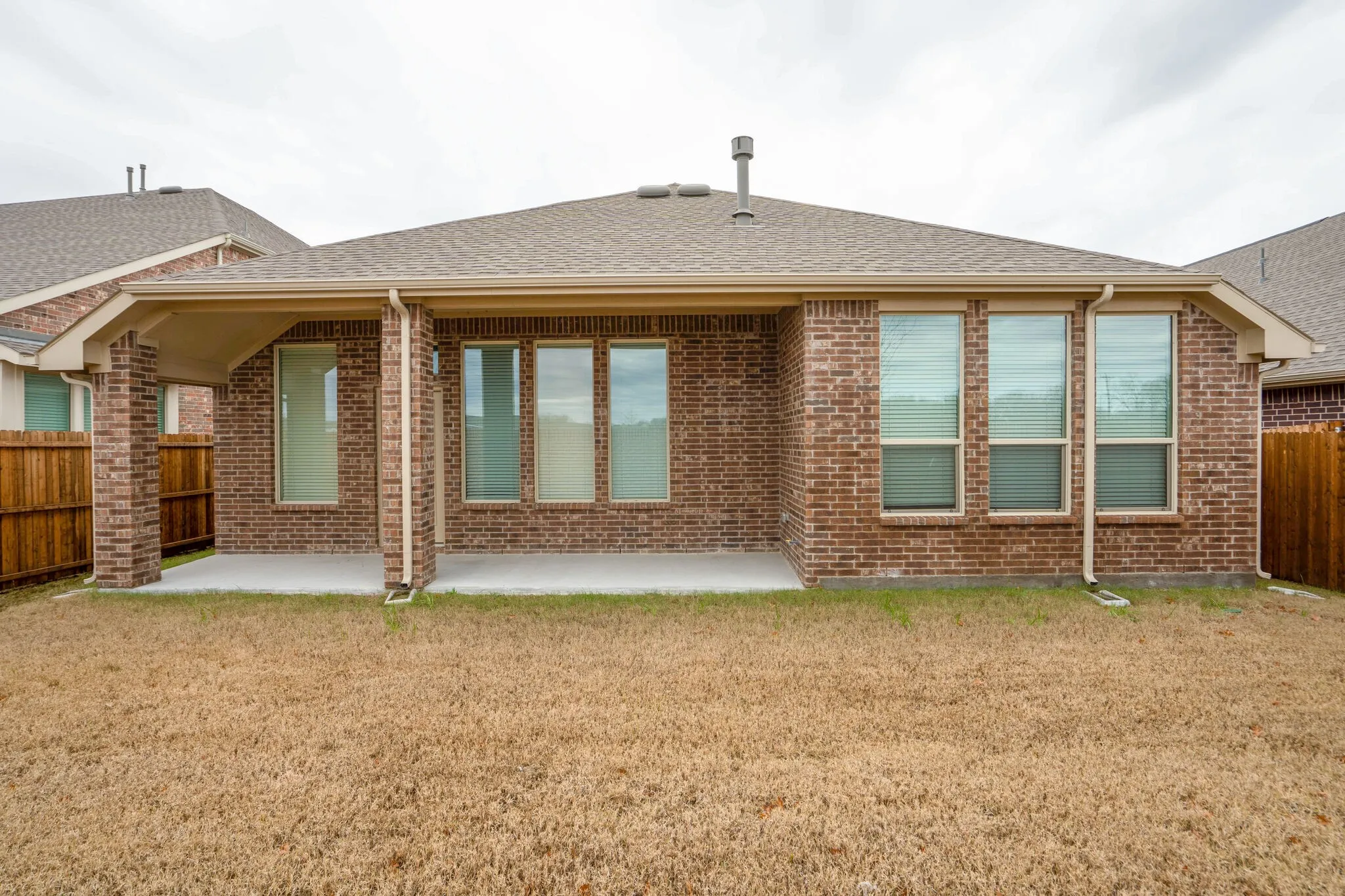 Brick exterior featuring a covered patio, multiple windows with blinds, and a fenced perimeter