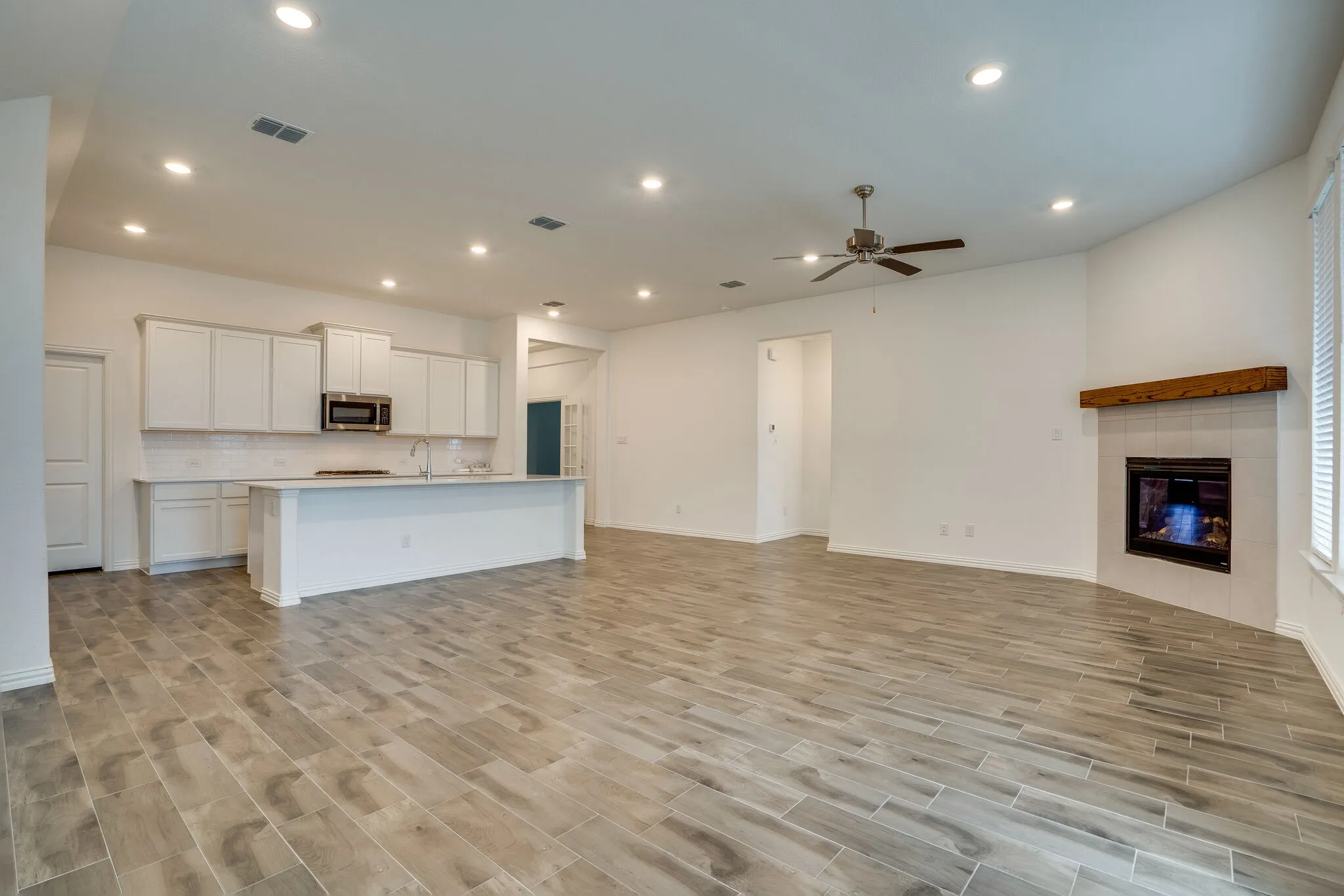 Open-concept living area with wood-finish tile flooring, recessed lighting, and a ceiling fan