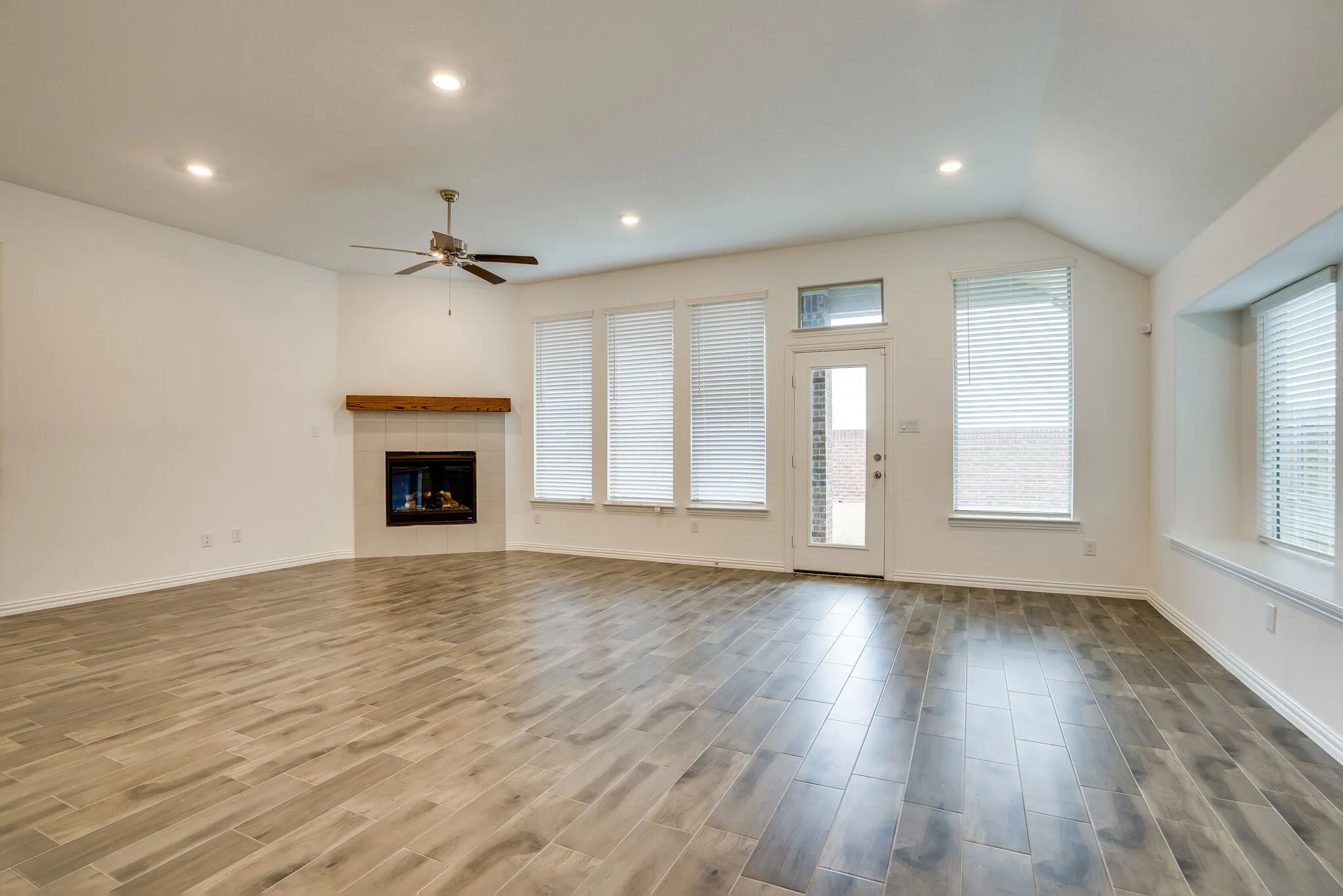 Spacious living area featuring wood-finish flooring, a corner fireplace with a wood mantle, and a ceiling fan