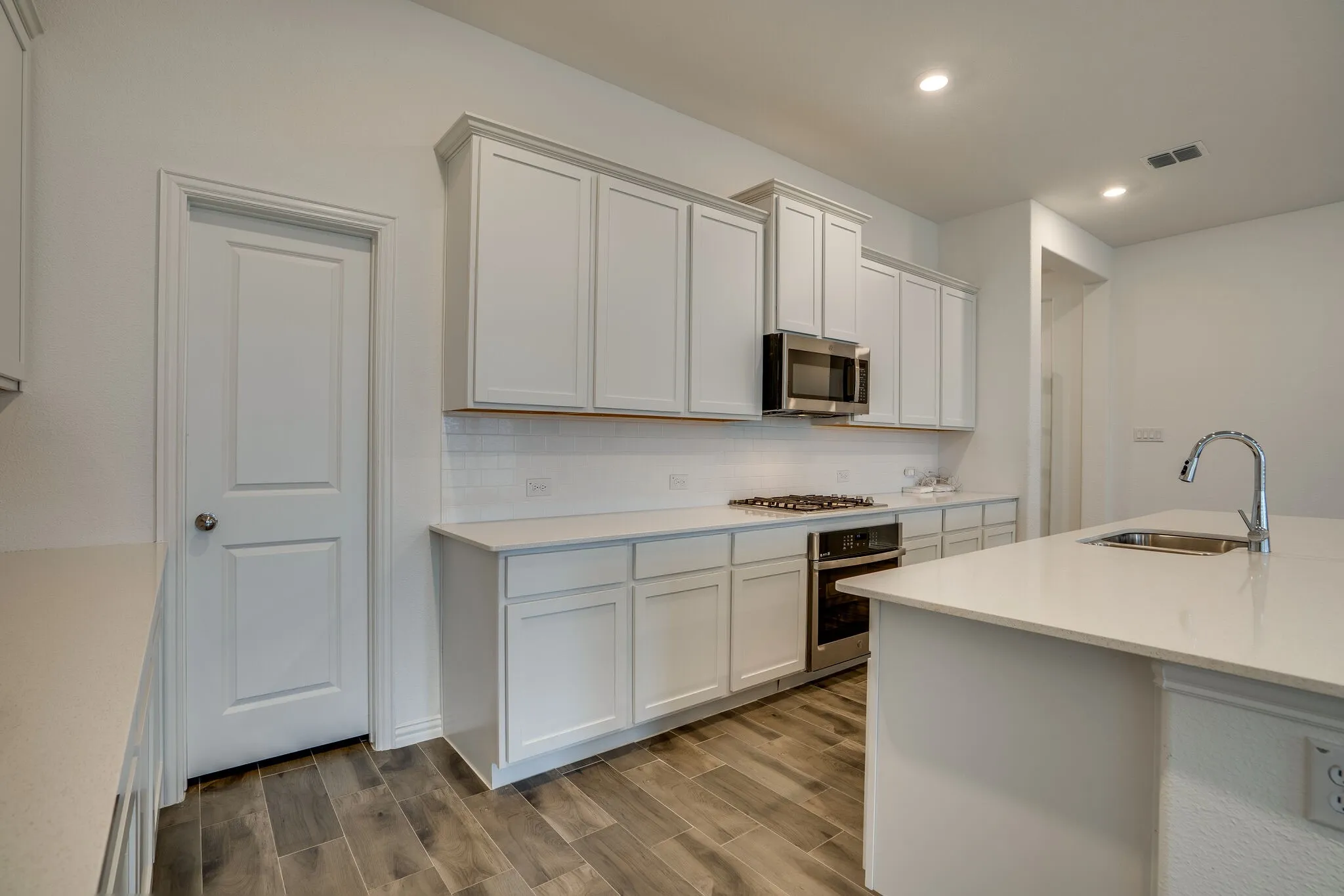 Modern kitchen featuring light cabinetry, stainless steel appliances, a gas range, white subway tile backsplash, and wood-finish flooring